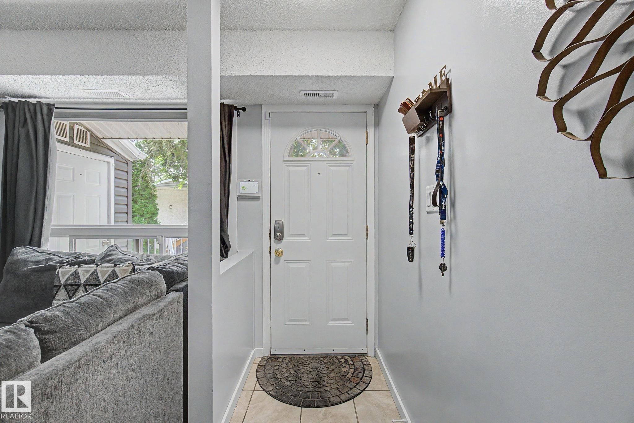 Entryway featuring a white door with an arched glass insert, light-toned tile flooring, and light gray wall finishes - #39 3111 142 Av Nw, Edmonton, AB - Indoor Photo Showing Other Room