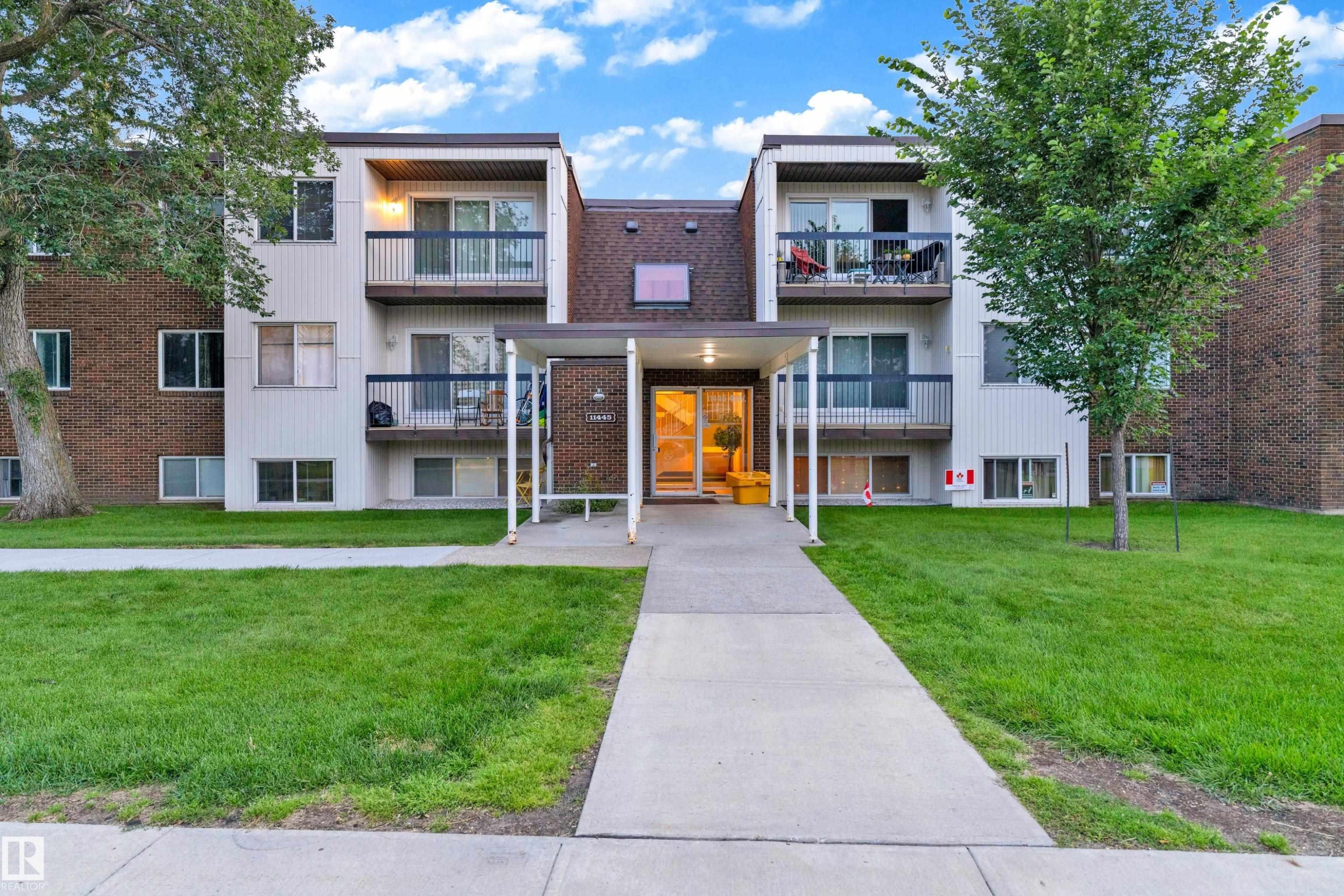 Multi-story residential building featuring brick and vertical siding, individual balconies, a covered entryway, and a concrete pathway - #104 11445 41 Av Nw, Edmonton, AB - Outdoor With Facade