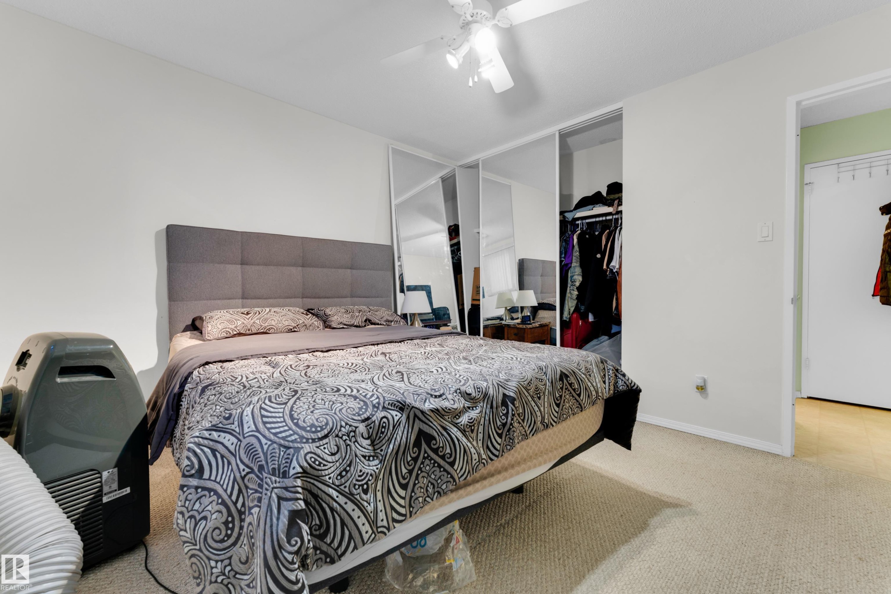Carpeted room featuring a ceiling fan, light-toned walls, and mirrored closet doors - #104 11445 41 Av Nw, Edmonton, AB - Indoor Photo Showing Bedroom