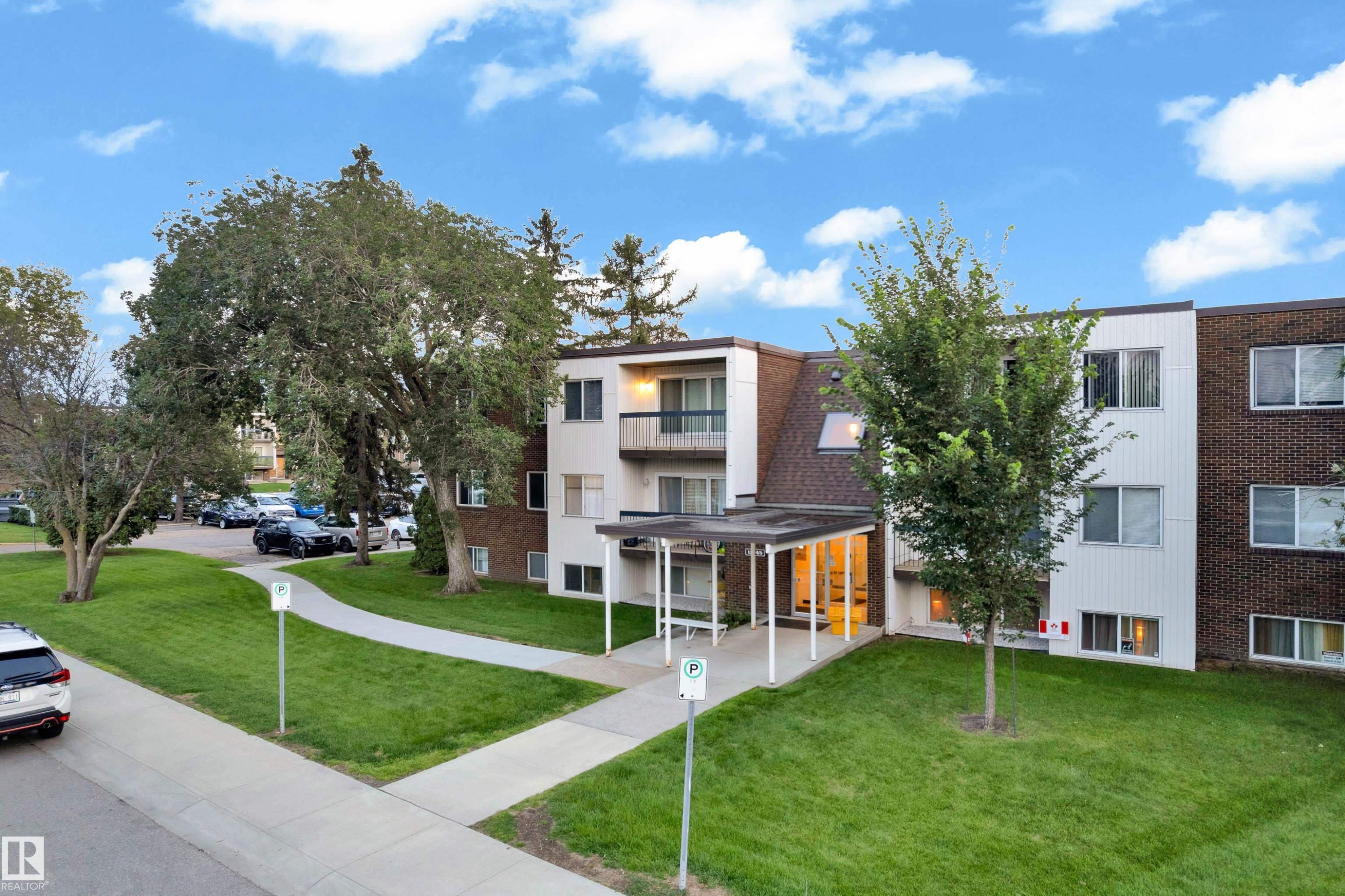 Multi-story building featuring a pitched shingle roof and a combination of white siding and dark brick exterior - #104 11445 41 Av Nw, Edmonton, AB - Outdoor With Facade