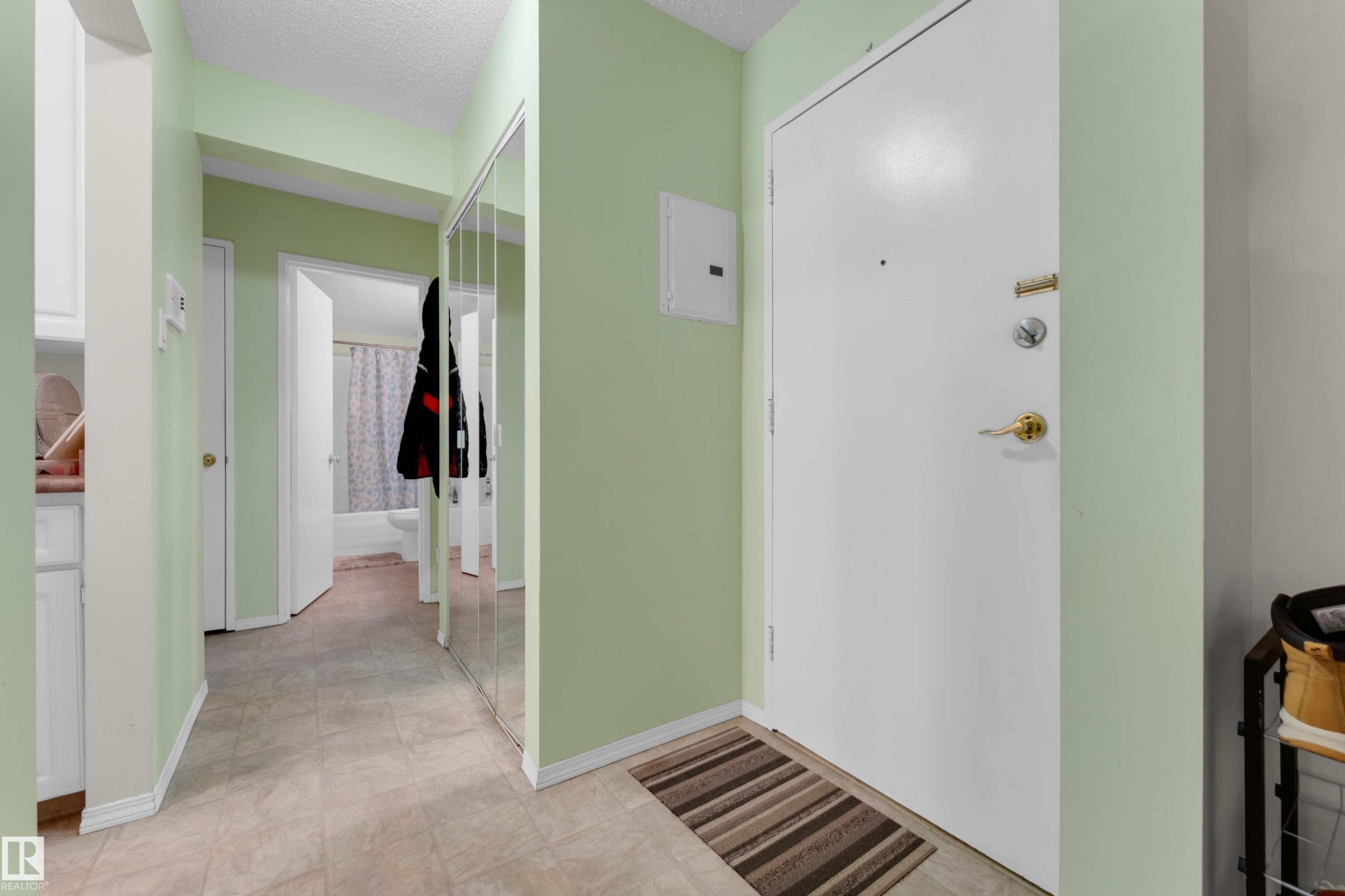 Entryway featuring a white solid door with brass hardware, light green walls, wood-finish flooring, and a mirrored closet door - #104 11445 41 Av Nw, Edmonton, AB - Indoor Photo Showing Other Room