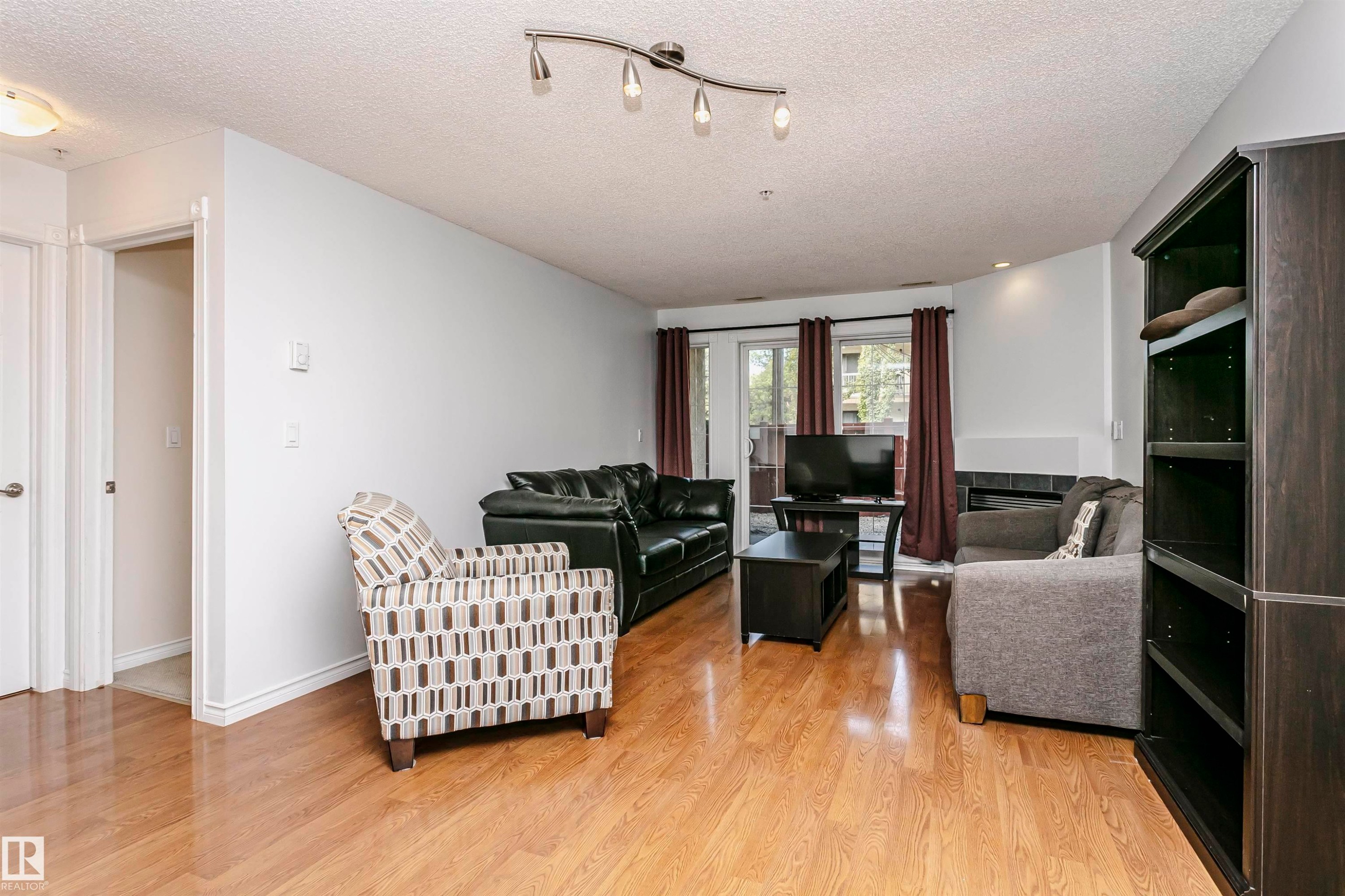 Open-concept living area featuring wood-finish flooring, a built-in fireplace with a tile surround, and a built-in dark wood shelving unit - #106 12110 106 Av Nw, Edmonton, AB - Indoor Photo Showing Living Room