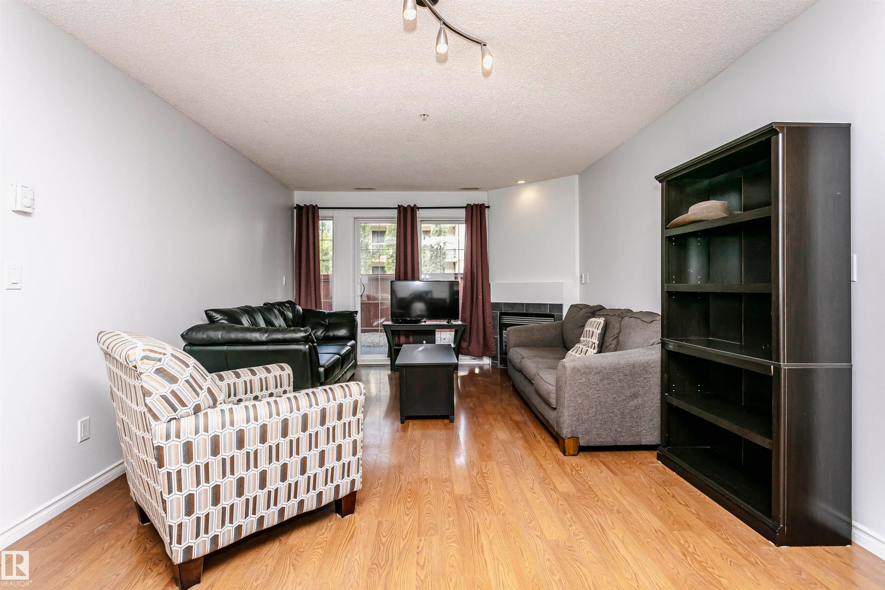 Living area featuring wood-finish flooring, light gray walls, and a recessed fireplace with dark tile surround - #106 12110 106 Av Nw, Edmonton, AB - Indoor Photo Showing Living Room