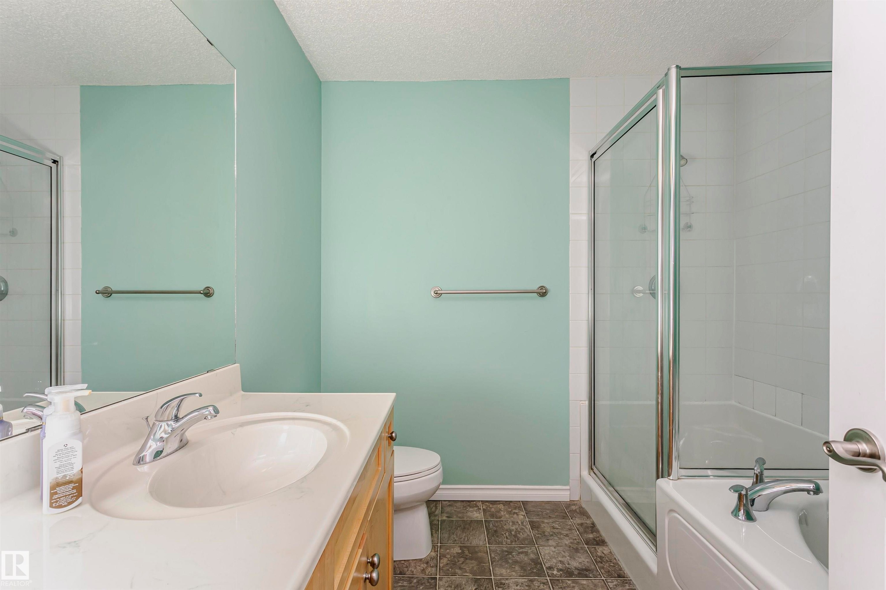 Bathroom featuring a shower-tub combination with glass enclosure, wood-finish vanity with an integrated sink, and a large wall-mounted mirror - #106 12110 106 Av Nw, Edmonton, AB - Indoor Photo Showing Bathroom