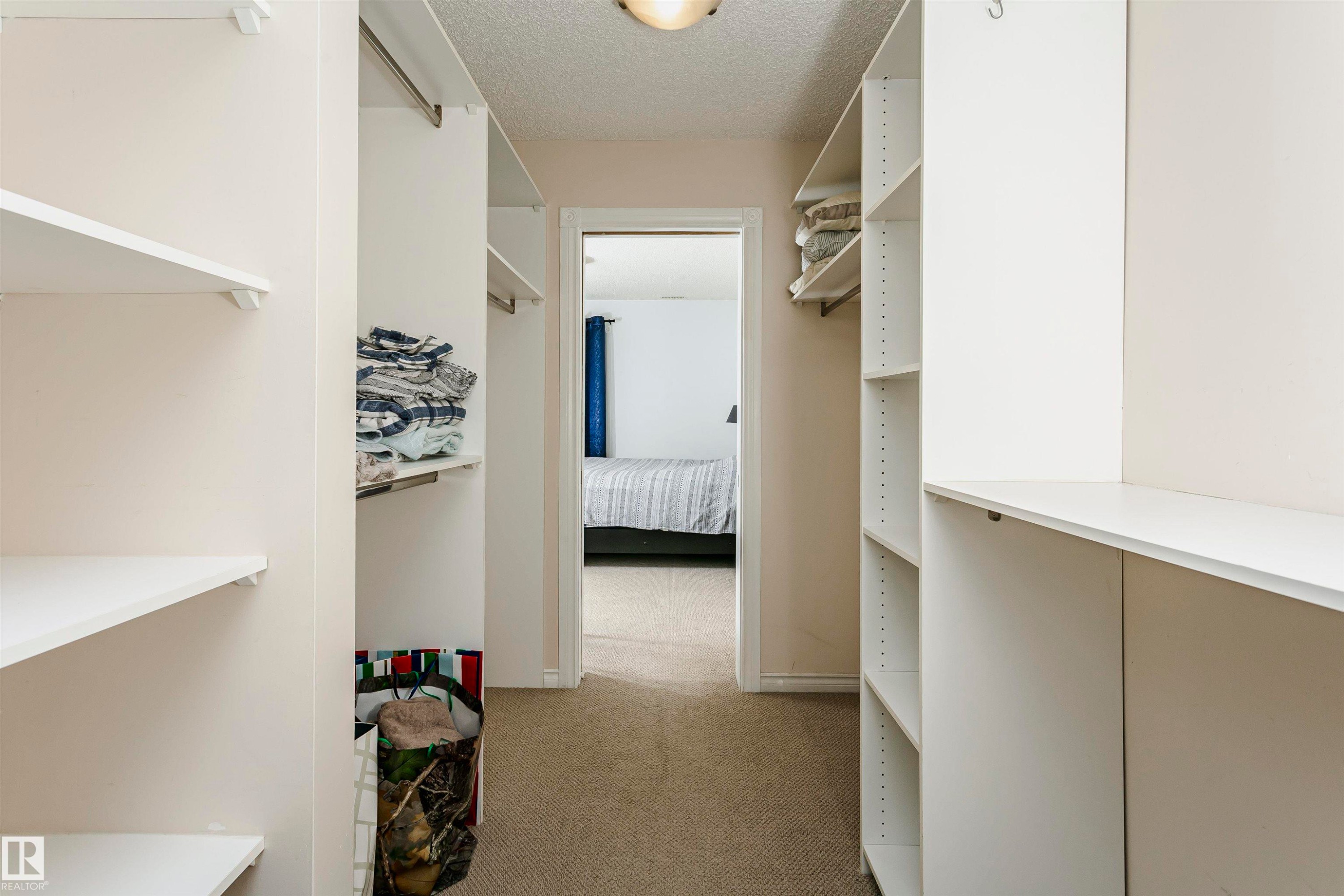 Walk-through closet featuring built-in white shelving, hanging rods, and carpet flooring - #106 12110 106 Av Nw, Edmonton, AB - Indoor