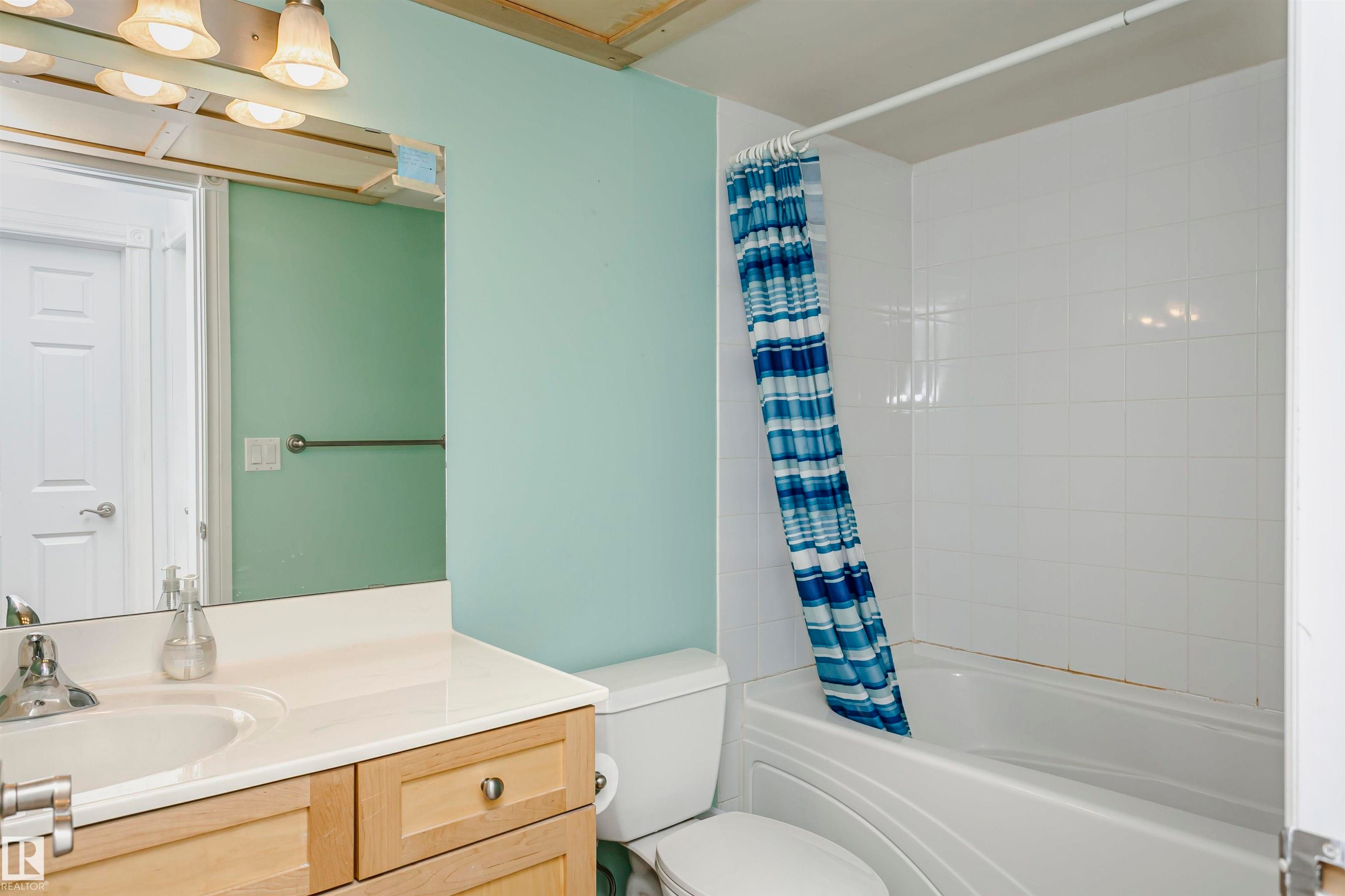 Bathroom featuring a light-toned vanity with an integrated sink, a white toilet, and a bathtub with white tiled surround - #106 12110 106 Av Nw, Edmonton, AB - Indoor Photo Showing Bathroom