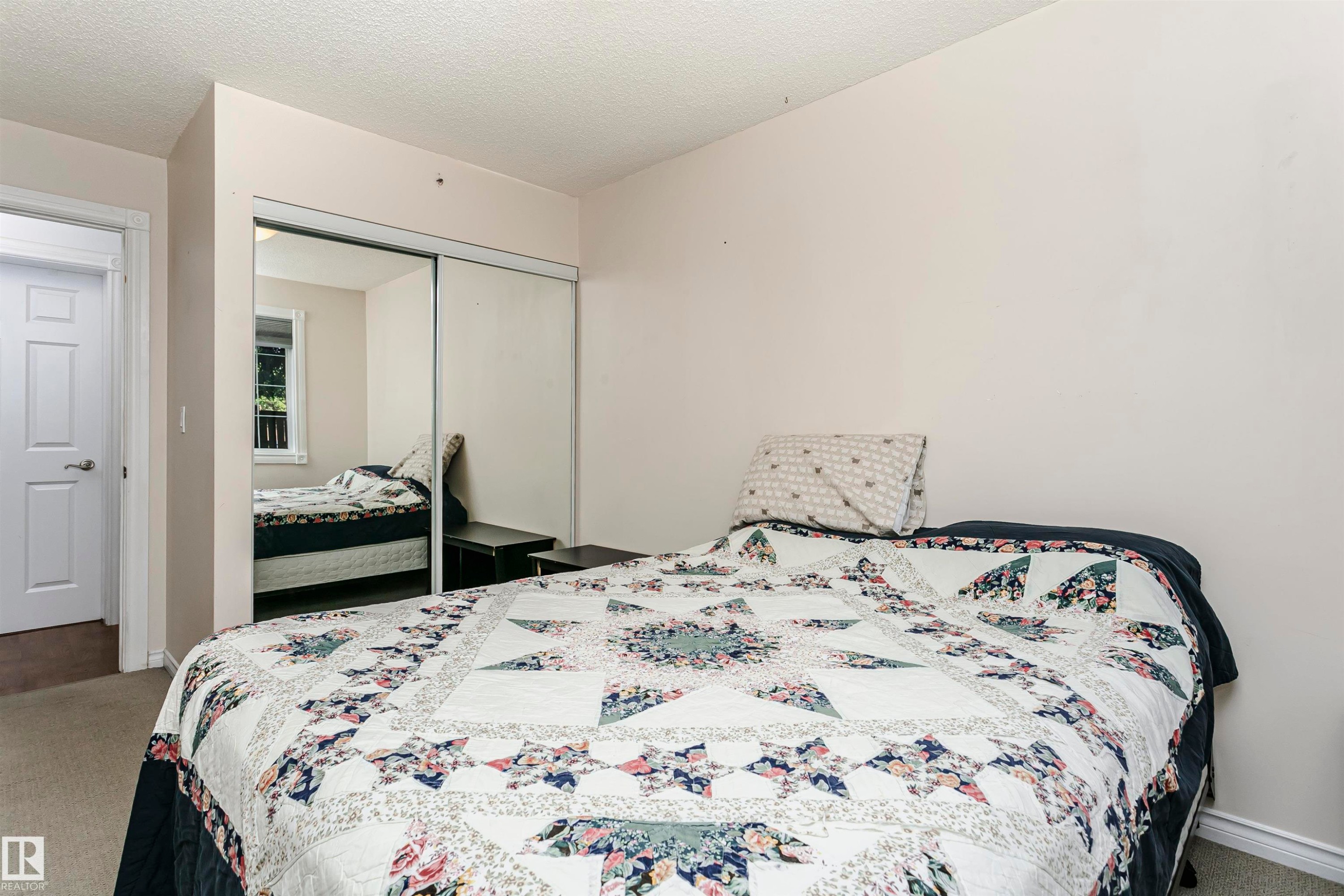 Bedroom featuring neutral wall colors, carpet flooring, a white paneled door, and a mirrored closet with sliding doors - #106 12110 106 Av Nw, Edmonton, AB - Indoor Photo Showing Bedroom