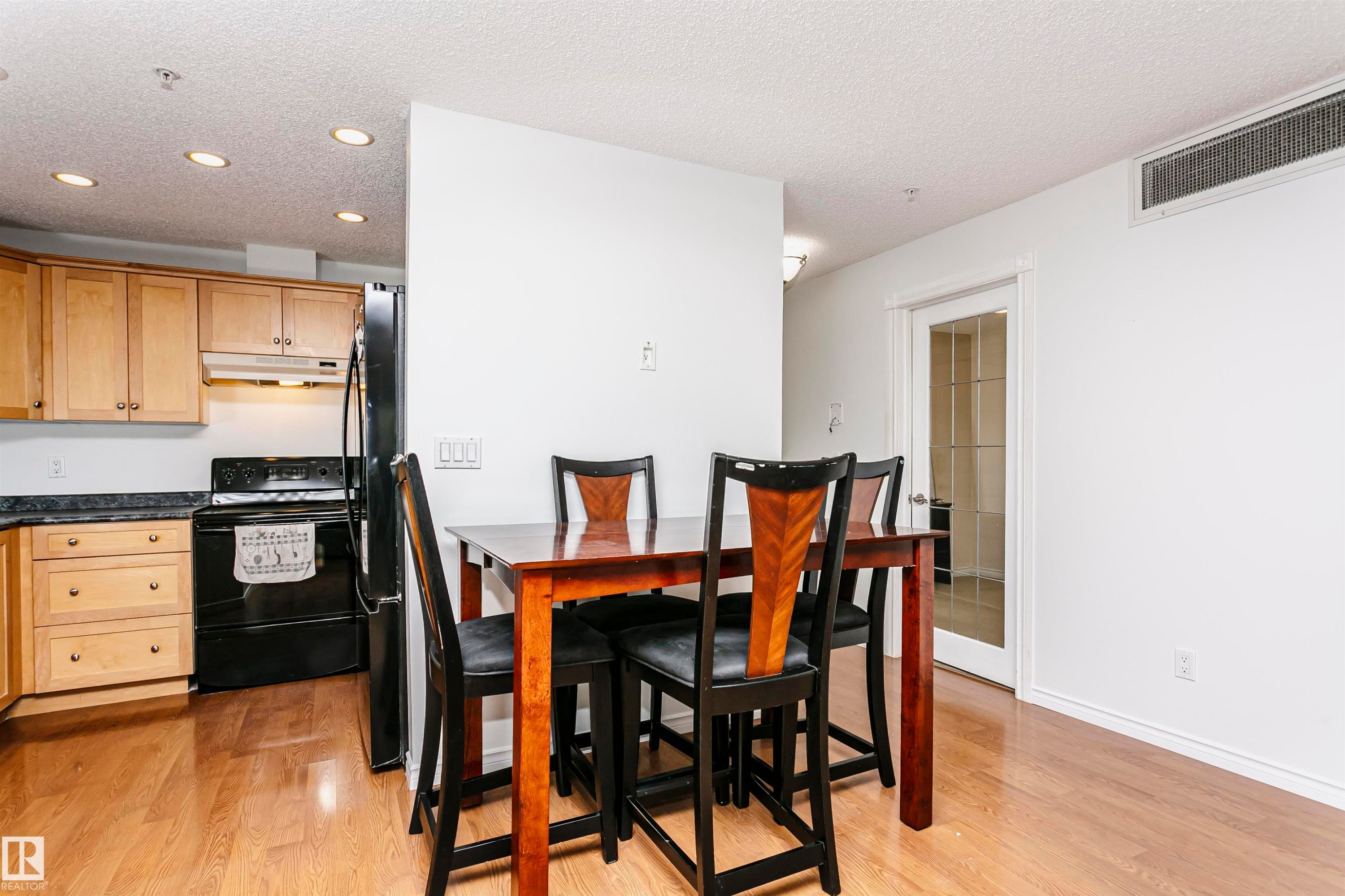 Kitchen and dining area featuring wood-finish flooring, recessed ceiling lighting, light wood cabinetry, dark countertops, and a full-size black refrigerator - #106 12110 106 Av Nw, Edmonton, AB - Indoor