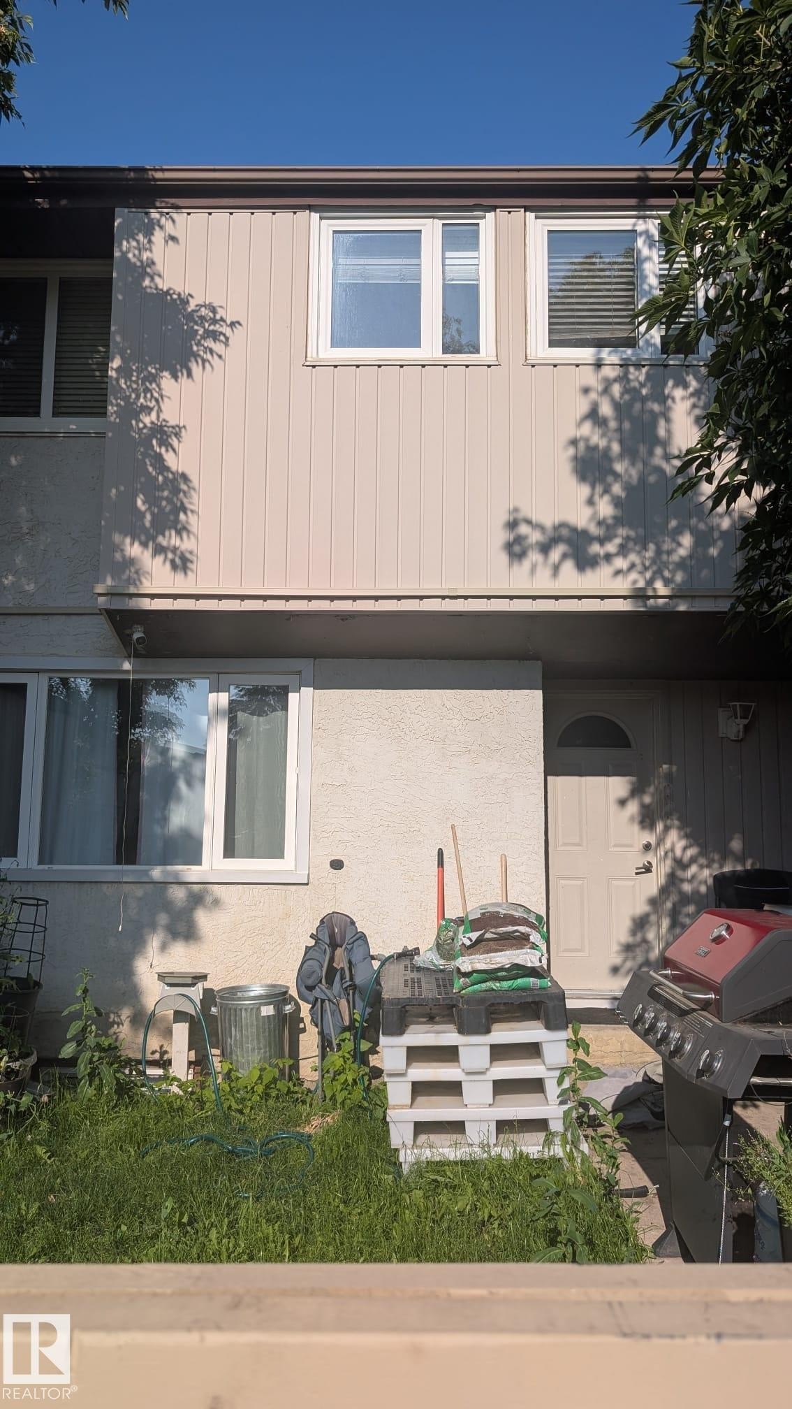 Two-story exterior featuring a ground-level entrance door, upper-level vertical siding, and multiple white-framed windows - #10 14220 80 St Nw, Edmonton, AB - Outdoor