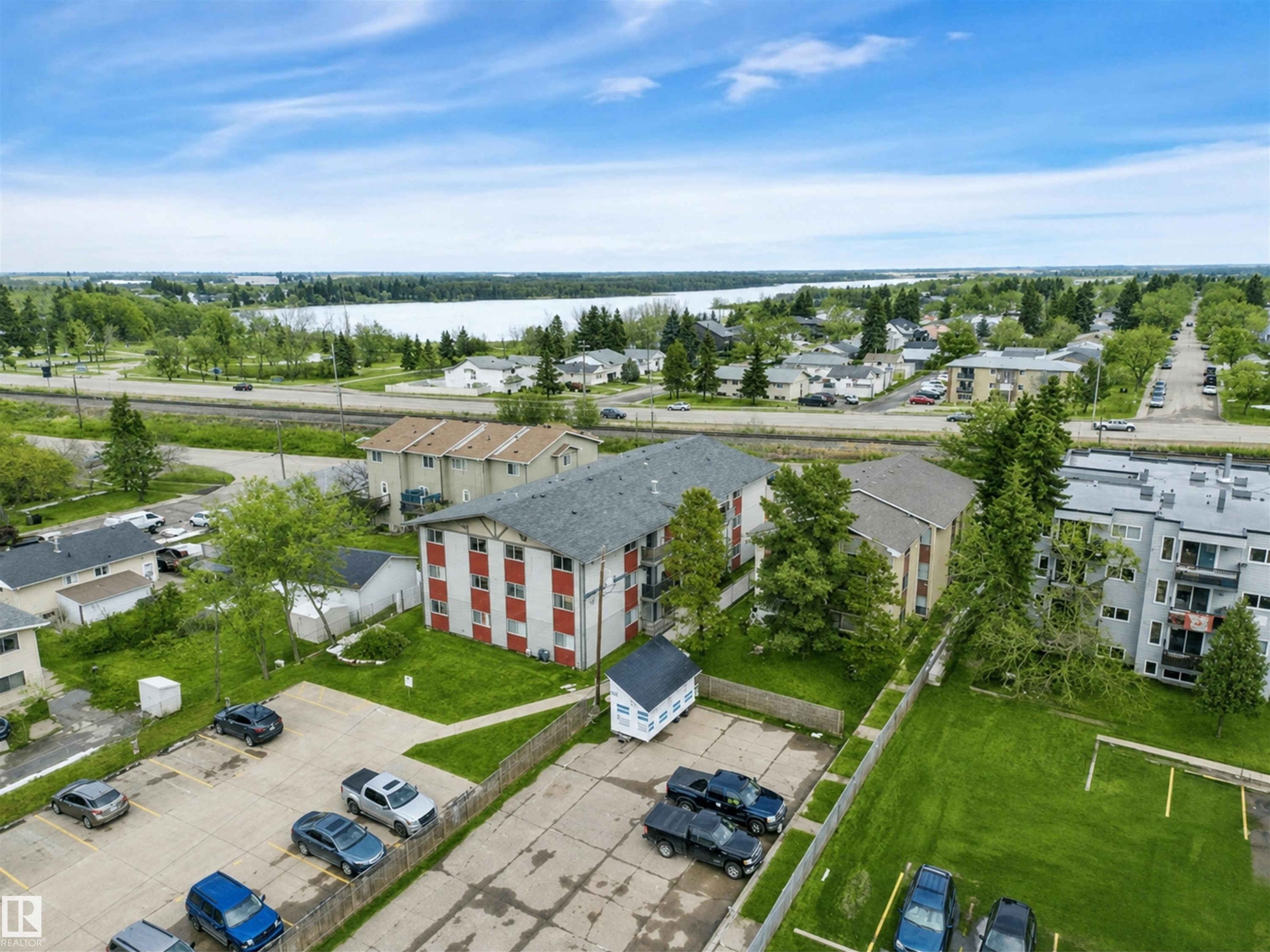Multi-story building featuring red and white exterior siding with a dark roof, surrounded by green landscaping - #10 4616 47 St, Leduc, AB - Outdoor With View