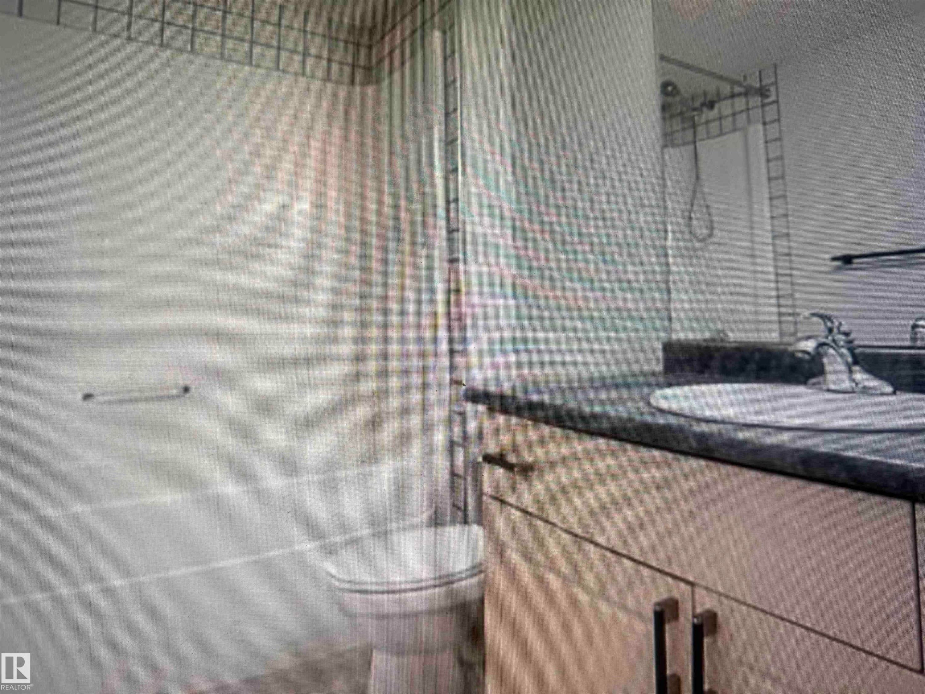Bathroom featuring a white tub-shower combination with grid-patterned wall tile, a single vanity with a dark countertop, an integrated sink, and brushed nickel fixtures - #106 592 Hooke Rd Nw, Edmonton, AB - Indoor Photo Showing Bathroom