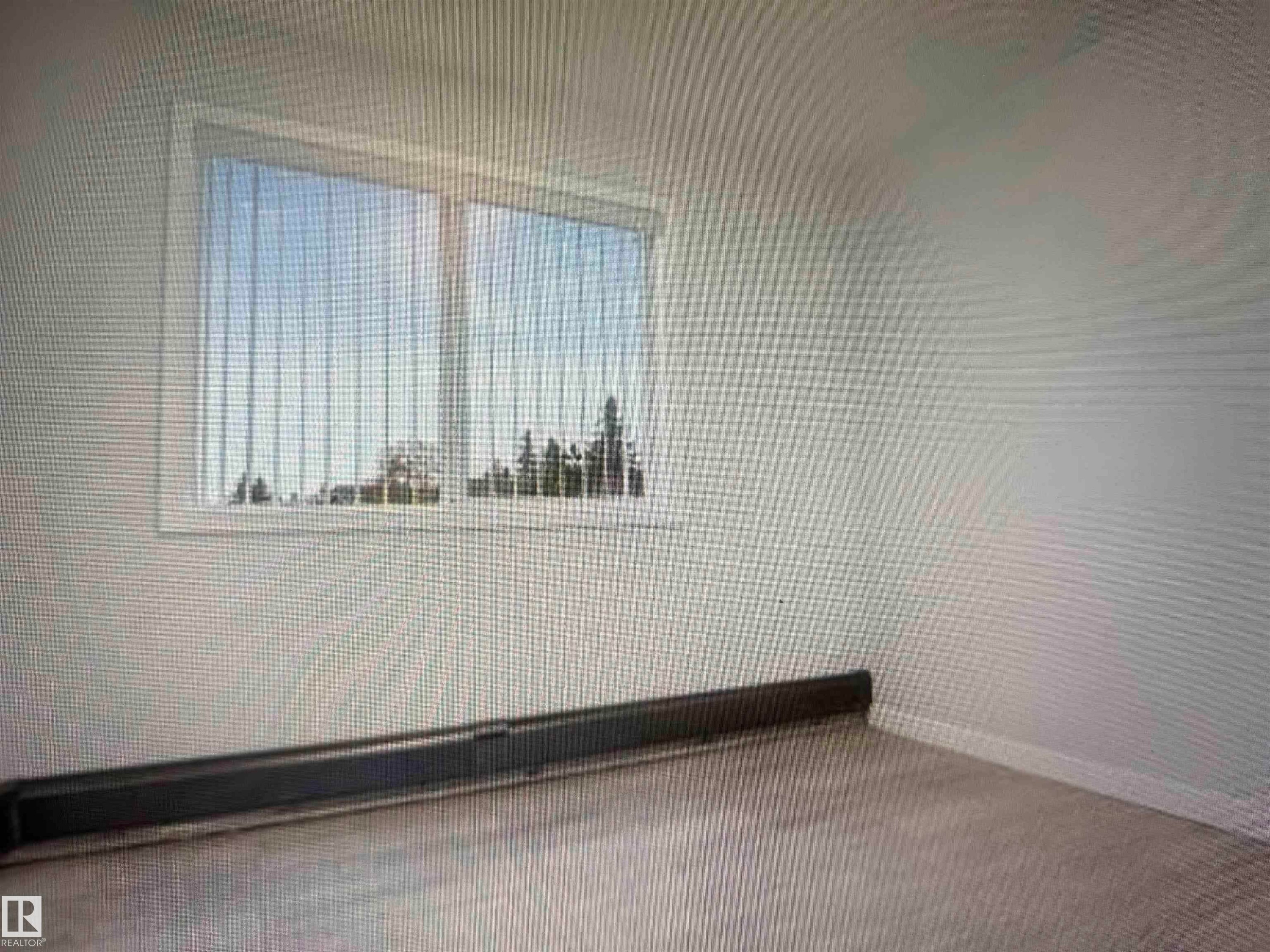Room featuring wood-finish flooring, a baseboard heating unit, and a window with vertical blinds - #106 592 Hooke Rd Nw, Edmonton, AB - Indoor Photo Showing Other Room