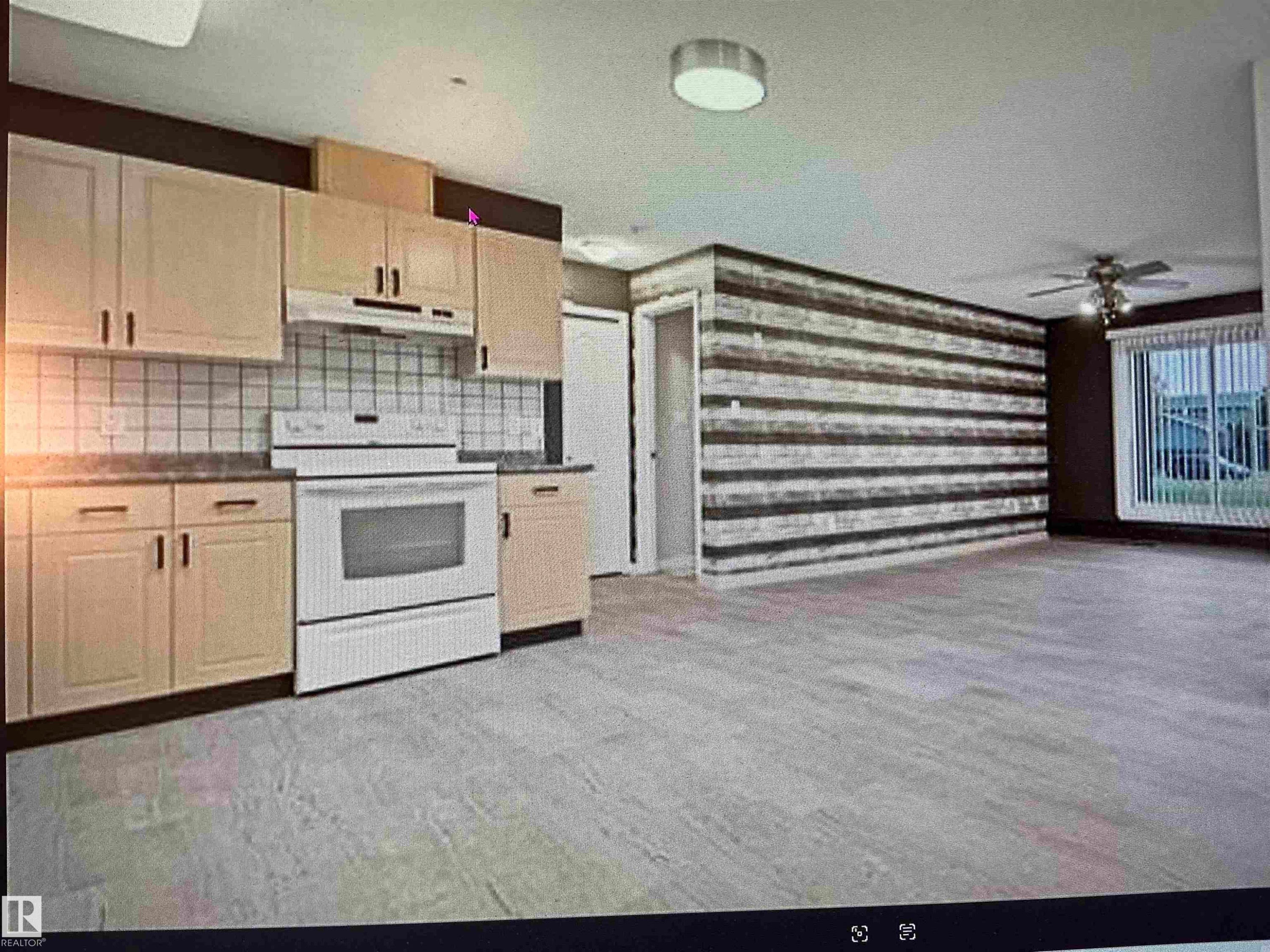 Open-concept kitchen and living area featuring light wood-finish cabinetry, white tile backsplash, a built-in electric range, and light-toned flooring - #106 592 Hooke Rd Nw, Edmonton, AB - Indoor Photo Showing Kitchen