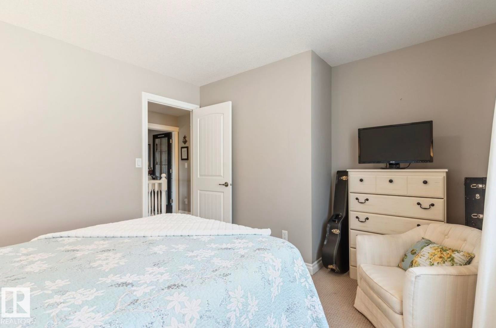 Neutral-toned bedroom featuring carpeted flooring and an open doorway leading to a hallway with a staircase - 22 Voleta Crest, Spruce Grove, AB - Indoor Photo Showing Bedroom