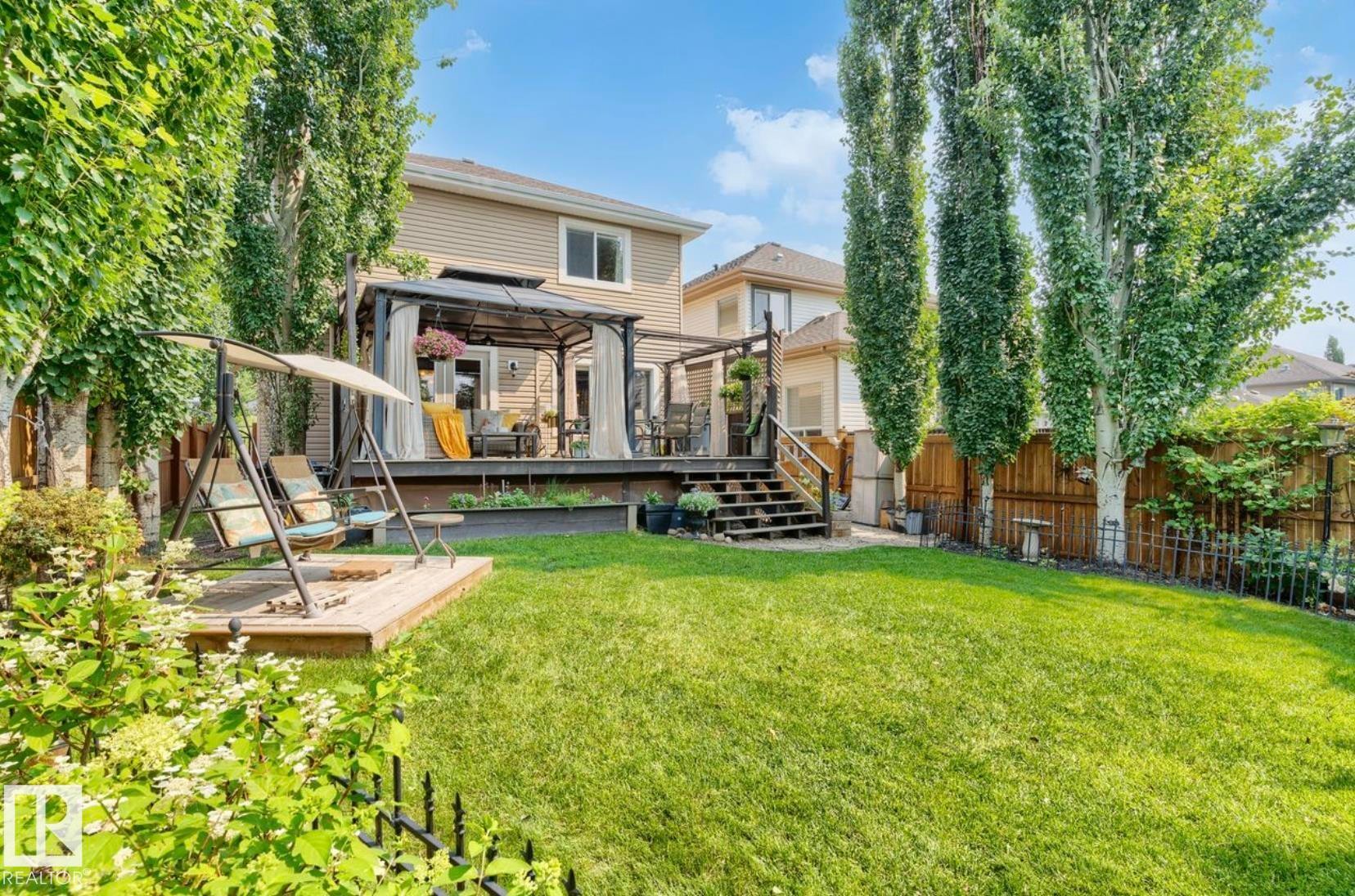 Expansive backyard oasis featuring a manicured lawn, mature poplar trees providing natural screening, and a composite deck with integrated pergola structure - 22 Voleta Crest, Spruce Grove, AB - Outdoor With Deck Patio Veranda