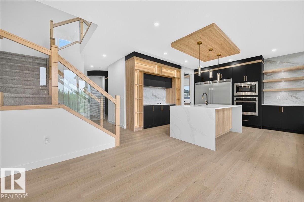 Gourmet kitchen with a waterfall island, integrated stainless steel appliances, modern black and wood-finish cabinetry, and a full-height marble-finish backsplash - 403 172 Avenue Nw, Edmonton, AB - Indoor Photo Showing Kitchen