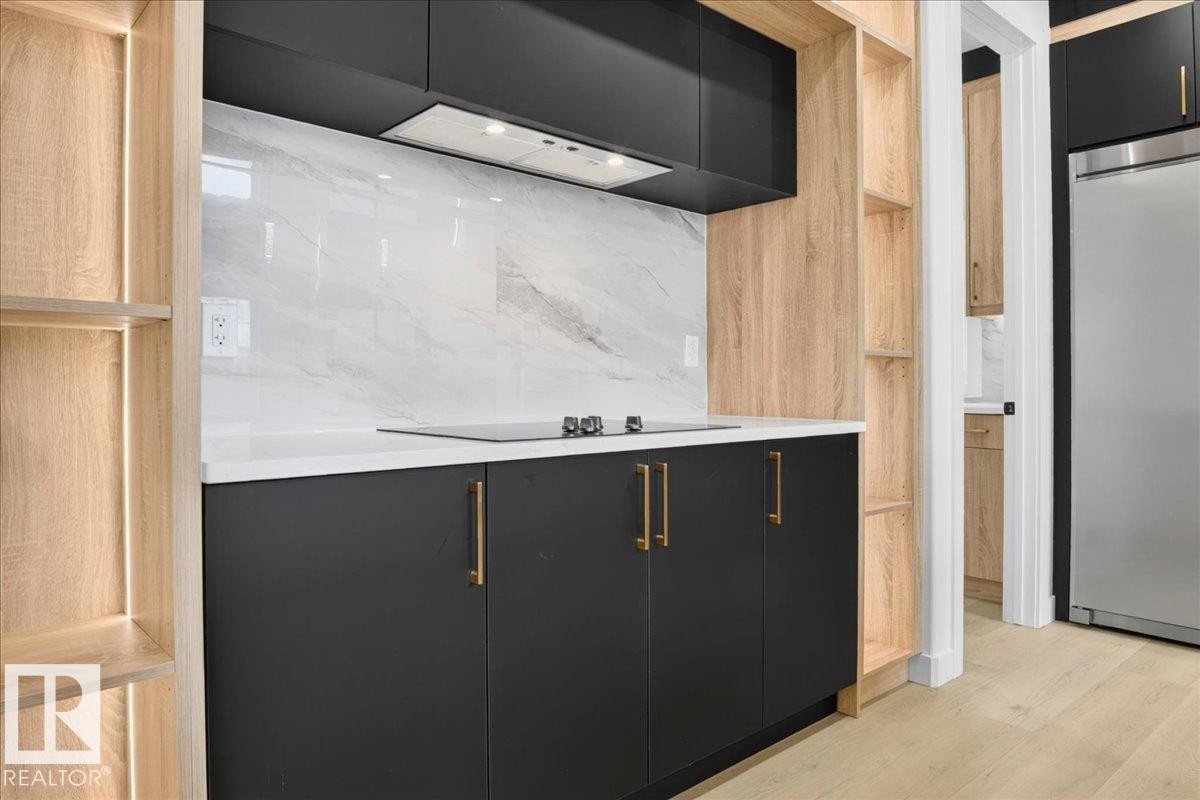 Kitchenette featuring black cabinetry with gold-tone hardware, white countertop, and a light-toned wood-finish open shelving system - 403 172 Avenue Nw, Edmonton, AB - Indoor