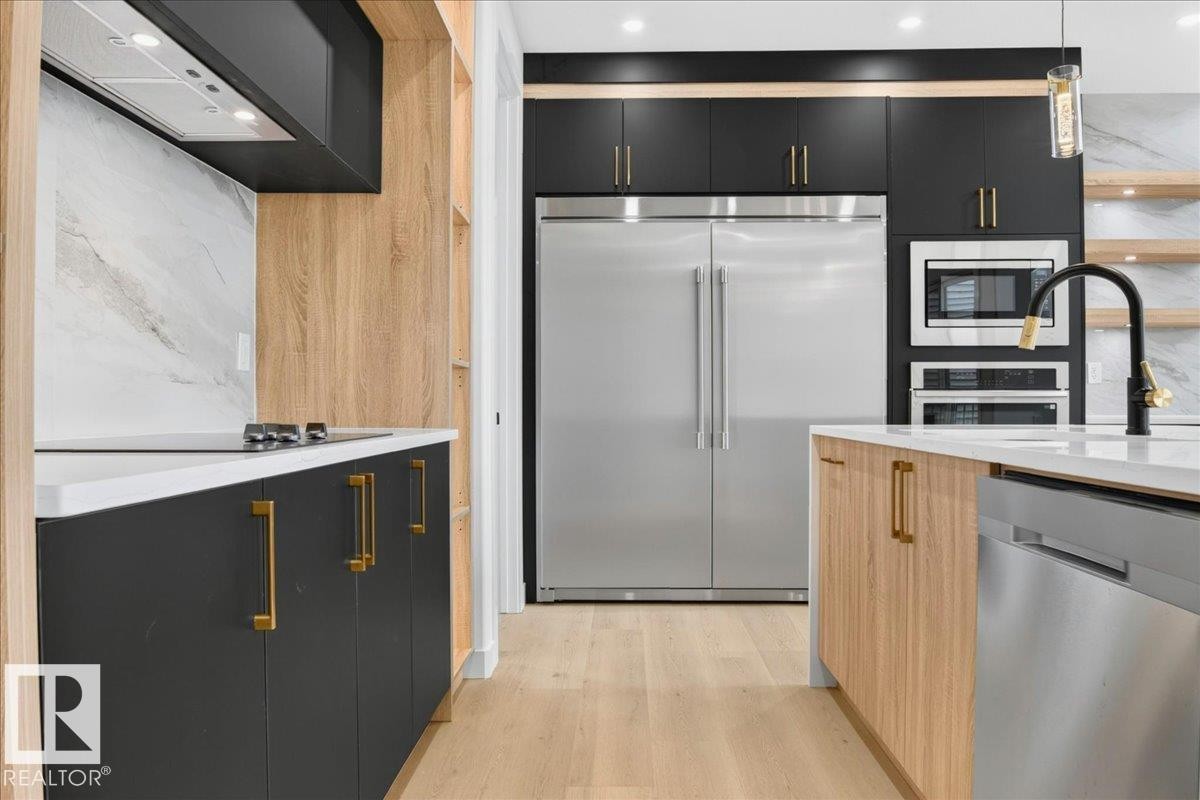 Contemporary kitchen featuring light wood-finish flooring, dark cabinetry with brass hardware, a stainless steel refrigerator, and integrated appliances - 403 172 Avenue Nw, Edmonton, AB - Indoor Photo Showing Kitchen