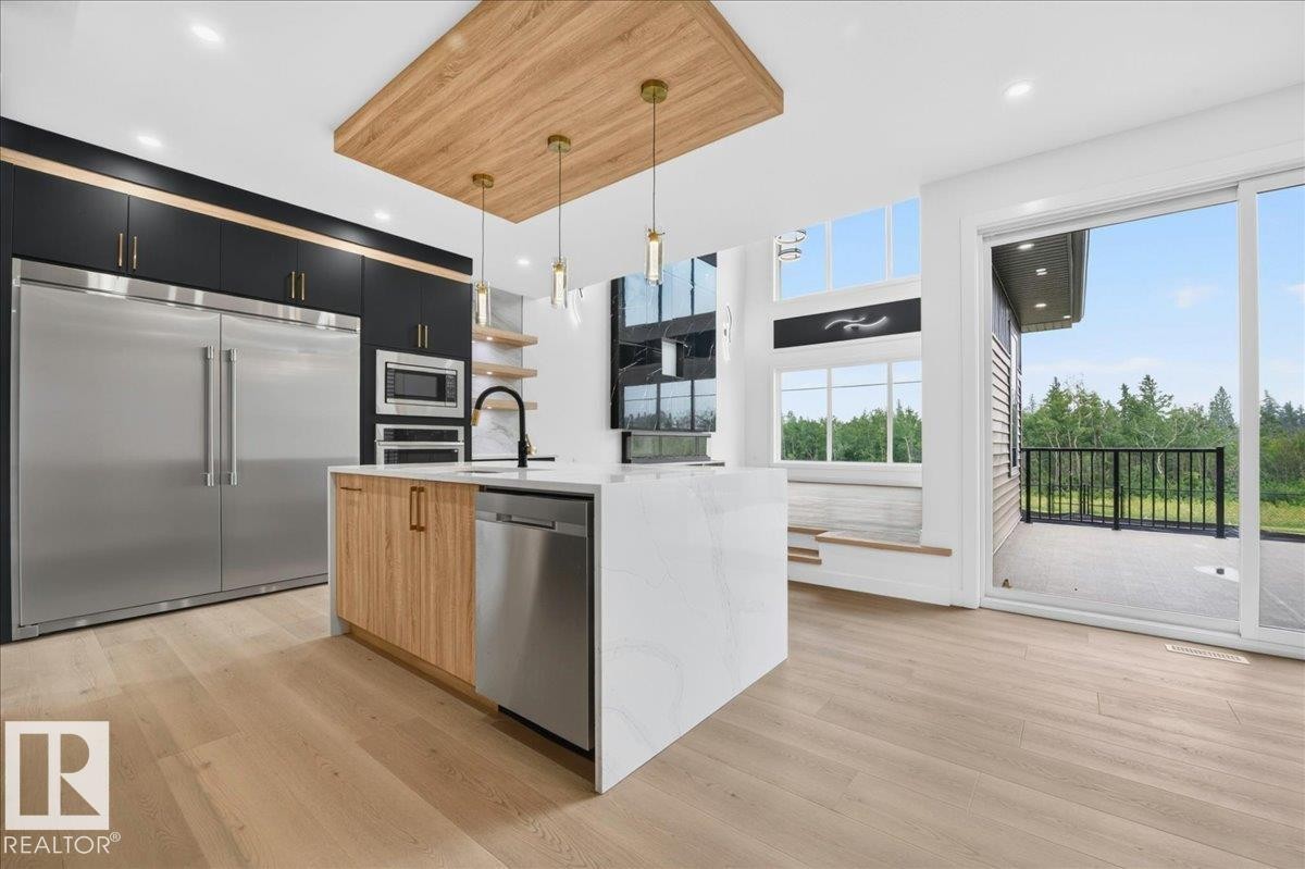 Contemporary kitchen featuring light wood-finish flooring, a waterfall island with a white countertop, and dark cabinetry with gold-toned hardware - 403 172 Avenue Nw, Edmonton, AB - Indoor Photo Showing Kitchen