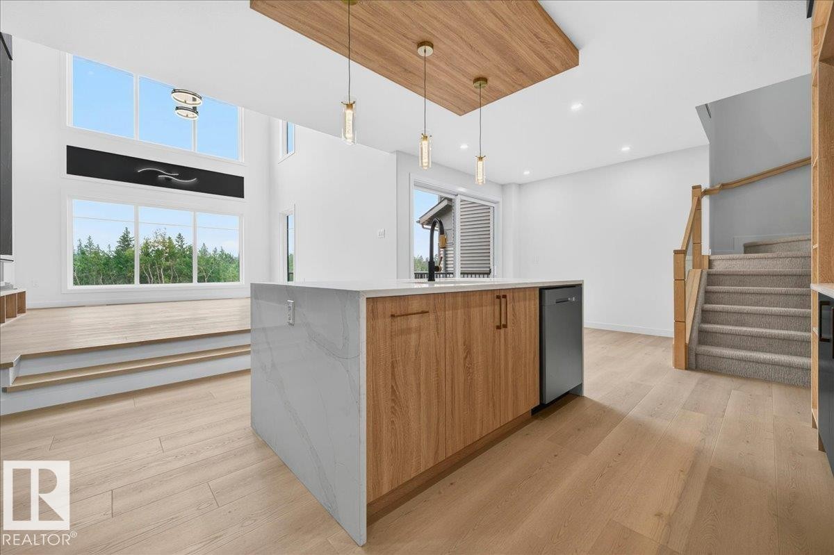 Open-concept interior featuring a central kitchen island with a waterfall countertop, integrated sink, and wood-finish cabinetry - 403 172 Avenue Nw, Edmonton, AB - Indoor Photo Showing Kitchen