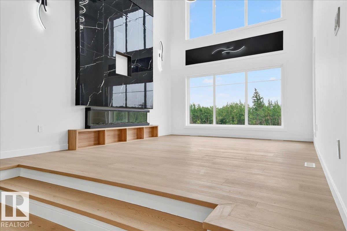 Two-story interior featuring light wood-finish flooring, a contemporary fireplace with a large black marble surround, an integrated linear electric fireplace, and a built-in wood-tone media console - 403 172 Avenue Nw, Edmonton, AB - Indoor Photo Showing Other Room