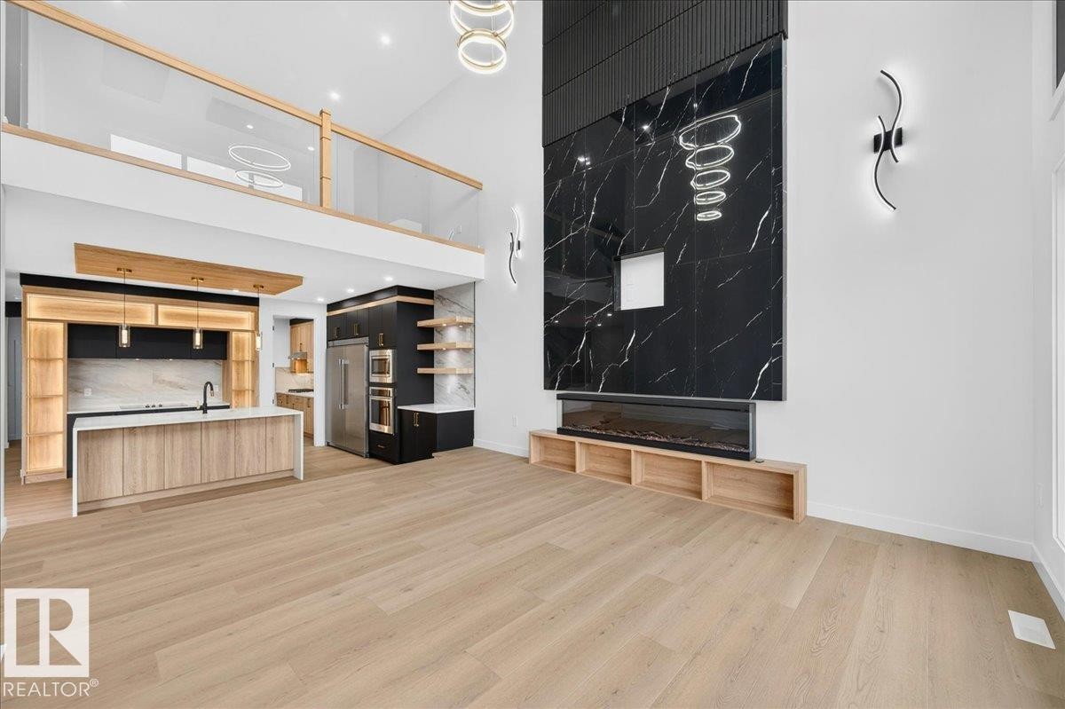 Open-concept living space featuring high ceilings, light wood-finish flooring, and a contemporary fireplace with a large-format black tile surround - 403 172 Avenue Nw, Edmonton, AB - Indoor