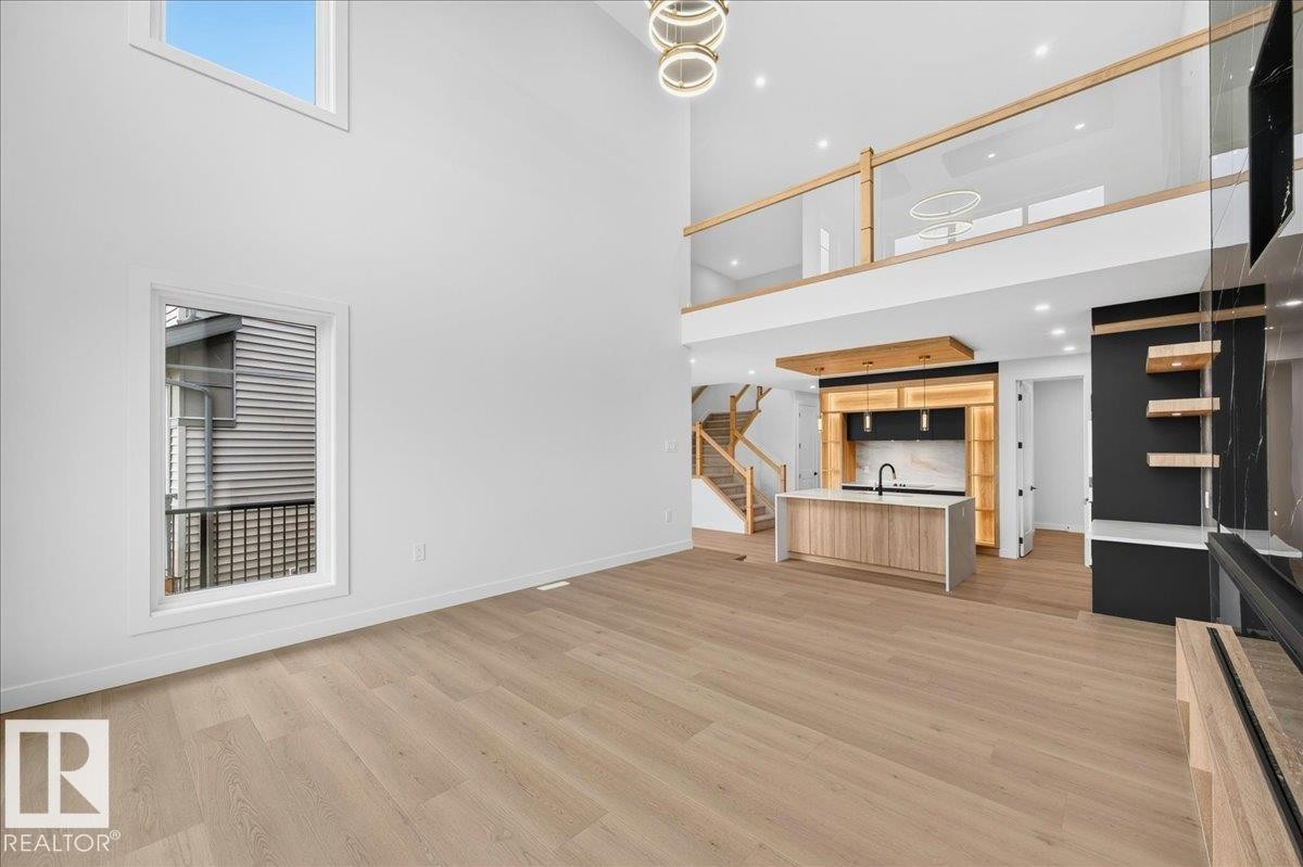 Open-concept living space featuring high ceilings, light wood-finish flooring, and a contemporary kitchen with an island - 403 172 Avenue Nw, Edmonton, AB - Indoor