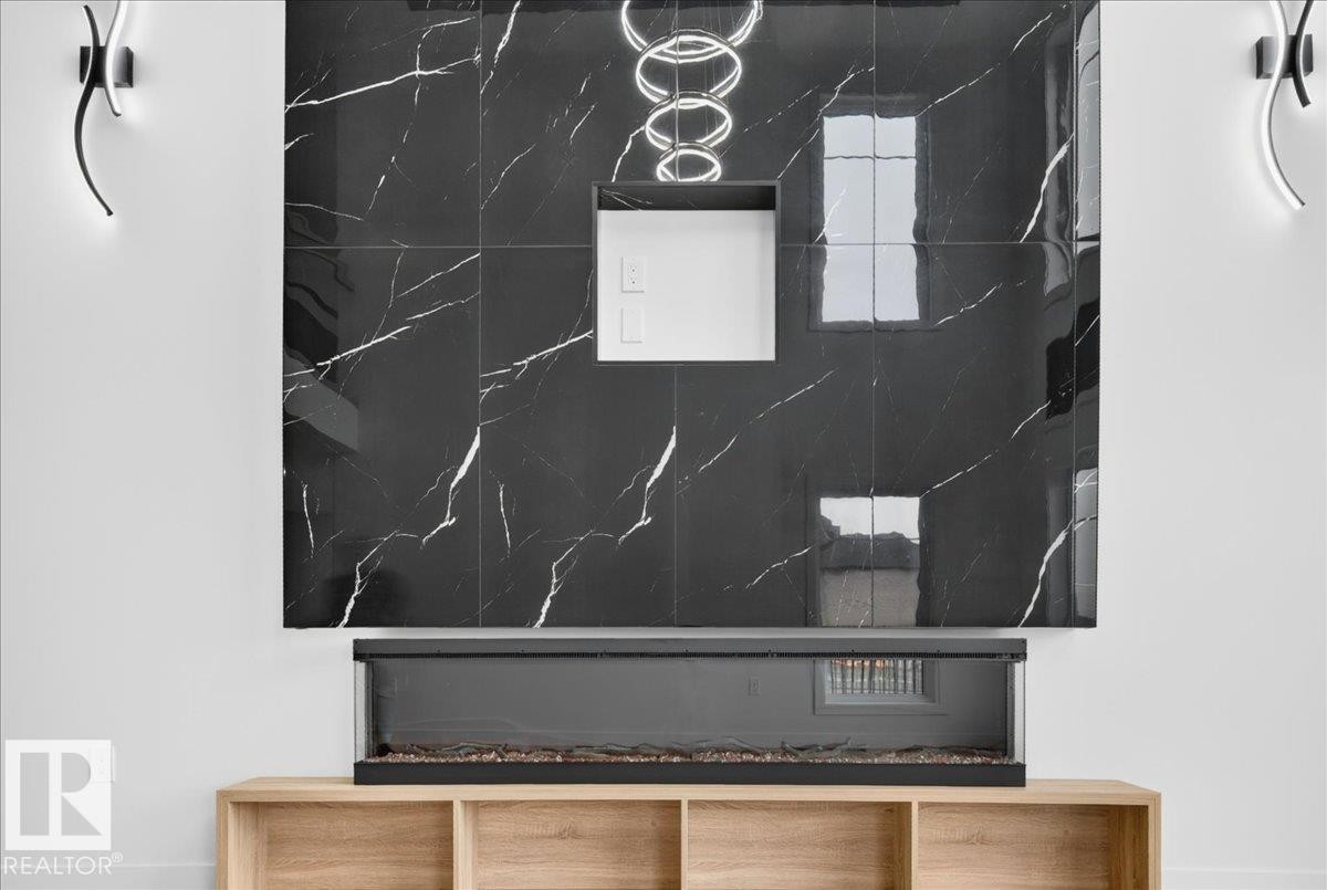 Striking feature wall with large format black marbled tiles, linear electric fireplace, built-in media niche, and recessed lighting - 403 172 Avenue Nw, Edmonton, AB - Other