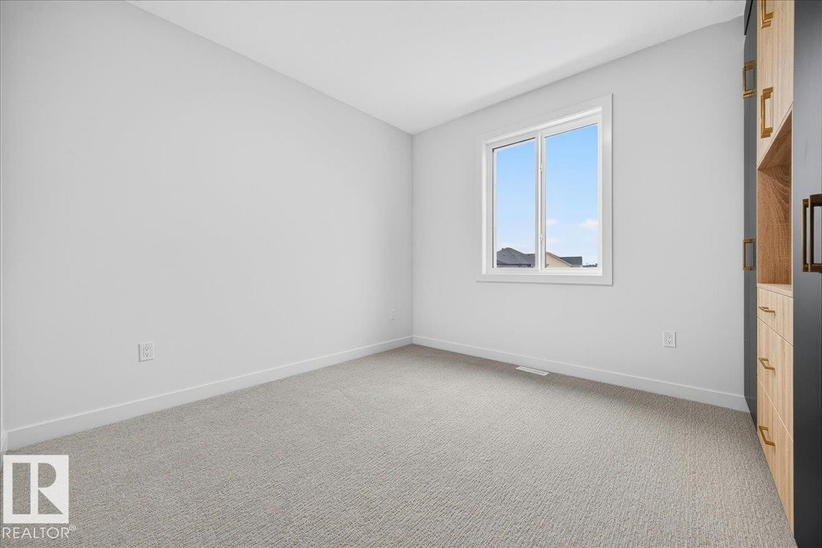 Light-filled interior space featuring a large window, neutral carpeting, and a built-in wardrobe with wood-finish cabinetry and dark accents - 403 172 Avenue Nw, Edmonton, AB - Indoor Photo Showing Other Room