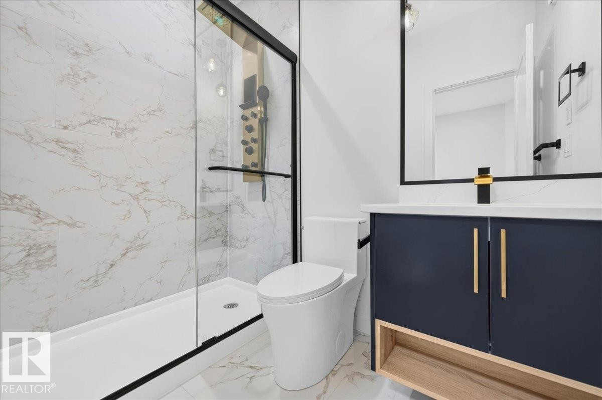 Modern bathroom featuring a walk-in shower with black-framed glass enclosure, white and gold veined wall and floor tiling, a dark blue vanity with gold hardware and white countertop, and a contemporary black and gold faucet - 403 172 Avenue Nw, Edmonton, AB - Indoor Photo Showing Bathroom