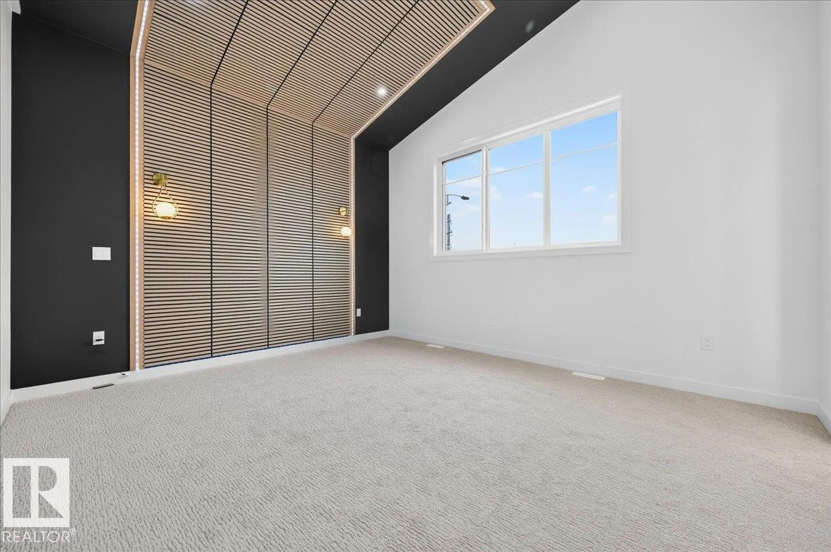 Vaulted ceiling room featuring a slatted wood-finish accent wall with integrated lighting, two wall sconces, and light-colored carpeting - 403 172 Avenue Nw, Edmonton, AB - Indoor Photo Showing Other Room