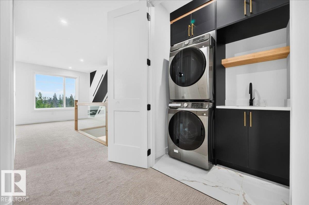Dedicated laundry area featuring stacked appliances, black cabinetry with gold-tone hardware, a light-toned countertop, and a black faucet - 403 172 Avenue Nw, Edmonton, AB - Indoor Photo Showing Laundry Room