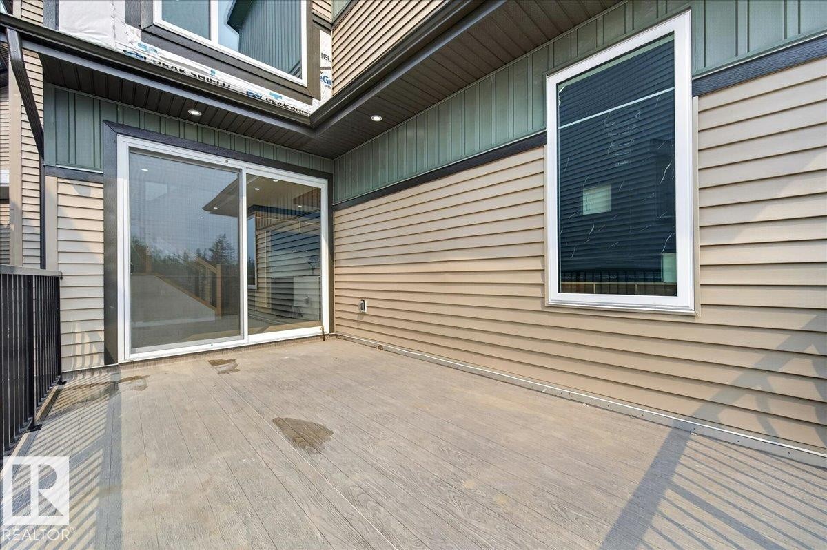 Outdoor patio with wood-finish flooring, featuring a large sliding glass door entry and black metal railings - 403 172 Avenue Nw, Edmonton, AB - Outdoor With Exterior