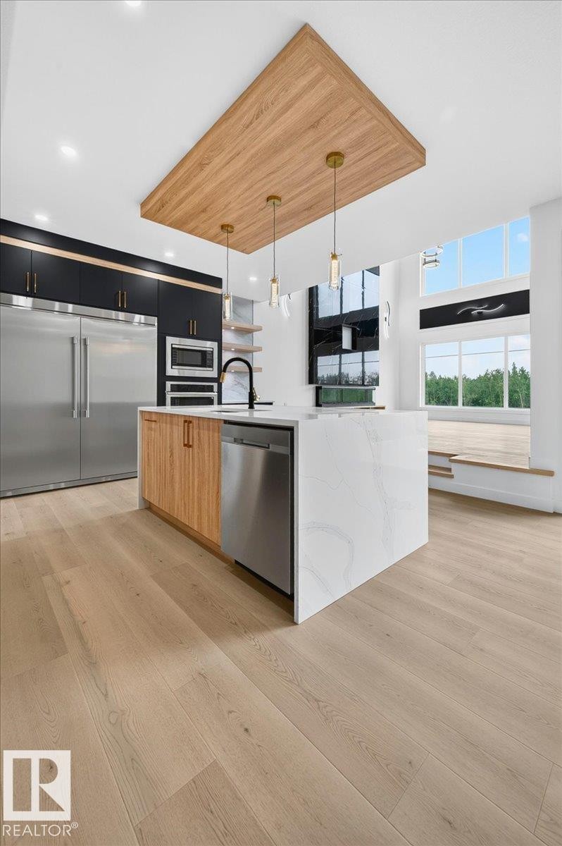 Modern kitchen featuring a waterfall-edge island with integrated dishwasher, stainless steel appliances, and a wood-finish ceiling accent with pendant lighting - 403 172 Avenue Nw, Edmonton, AB - Indoor Photo Showing Kitchen