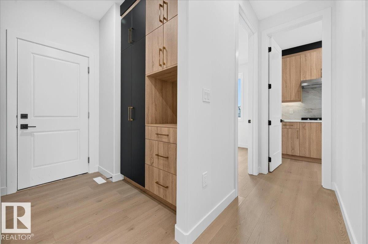 Entryway featuring wood-finish flooring, a white paneled door with black hardware, and a built-in storage unit with black and wood-tone cabinetry - 403 172 Avenue Nw, Edmonton, AB - Indoor Photo Showing Other Room