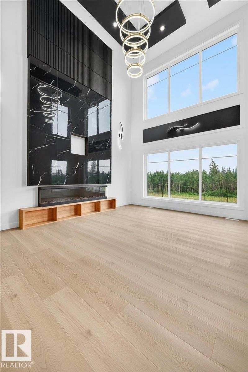 Open-concept living space featuring a floor-to-ceiling black marble-look fireplace surround, light wood-finish flooring, and a contemporary chandelier with stacked circular rings - 403 172 Avenue Nw, Edmonton, AB - Indoor Photo Showing Other Room