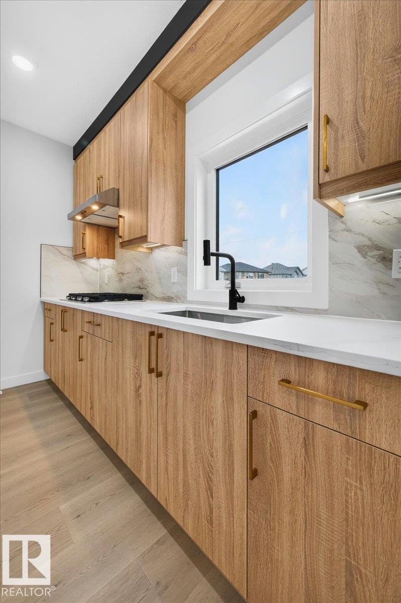 Modern kitchen featuring wood-finish cabinetry, white countertops, and a white tile backsplash - 403 172 Avenue Nw, Edmonton, AB - Indoor Photo Showing Kitchen