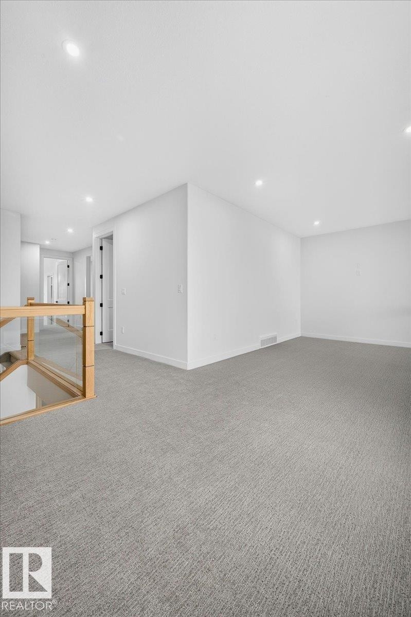 Spacious carpeted landing area with recessed lighting, white walls, and a light wood and glass panel railing - 403 172 Avenue Nw, Edmonton, AB - Indoor