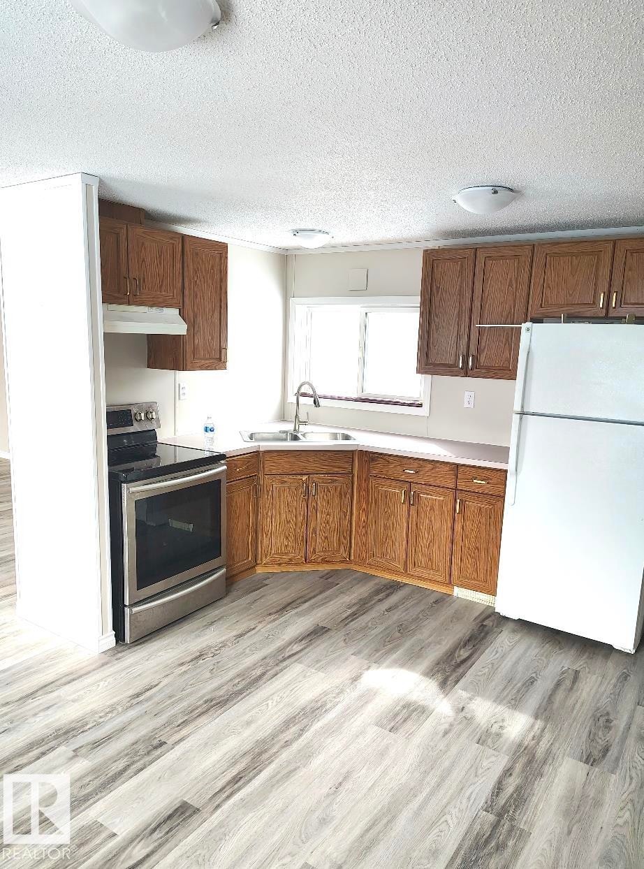 Kitchen featuring wood-finish cabinetry, light-toned countertops, a stainless steel electric range, and wood-finish flooring - 4819 51 Avenue, Millet, AB - Indoor Photo Showing Kitchen With Double Sink