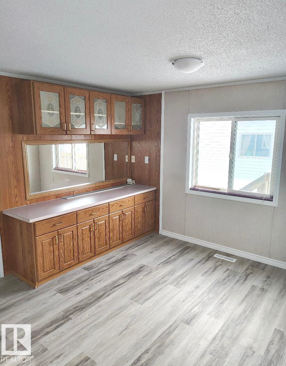 Light wood-finish flooring complements the built-in cabinetry with glass-front uppers and a mirrored backsplash - 4819 51 Avenue, Millet, AB - Indoor