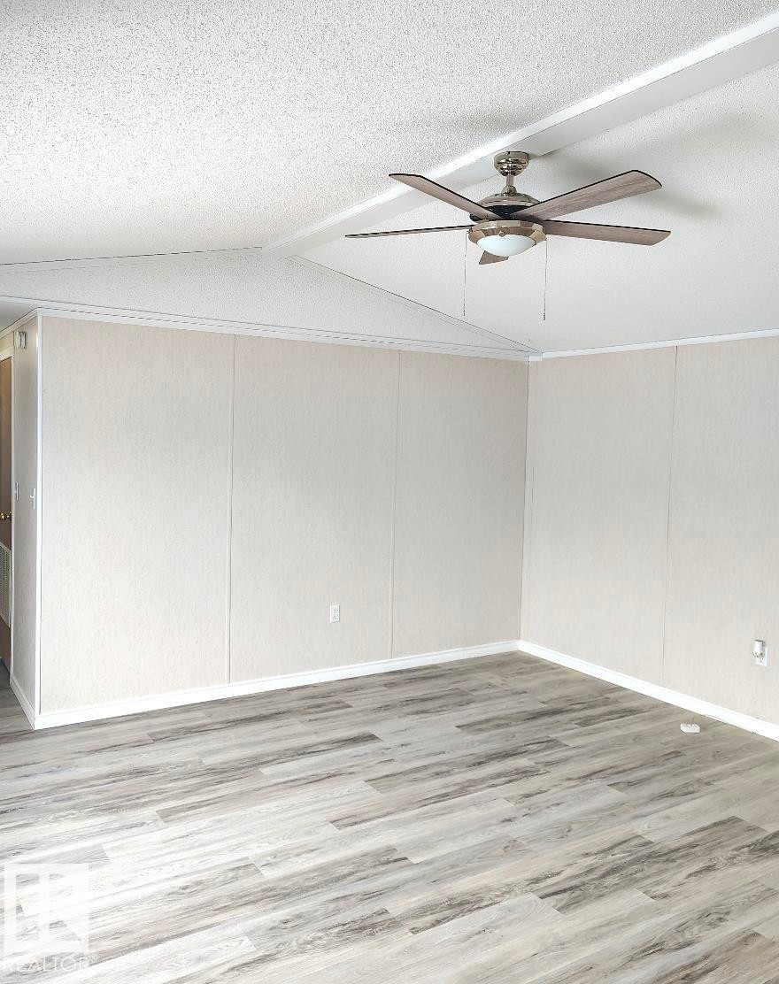 Spacious interior room featuring wood-finish flooring, light-toned wall paneling, and a contemporary ceiling fan with integrated lighting - 4819 51 Avenue, Millet, AB - Indoor Photo Showing Other Room
