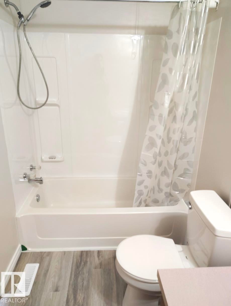 Bathroom featuring a white bathtub with an integrated shower, wood-finish flooring, and a white toilet - 4819 51 Avenue, Millet, AB - Indoor Photo Showing Bathroom