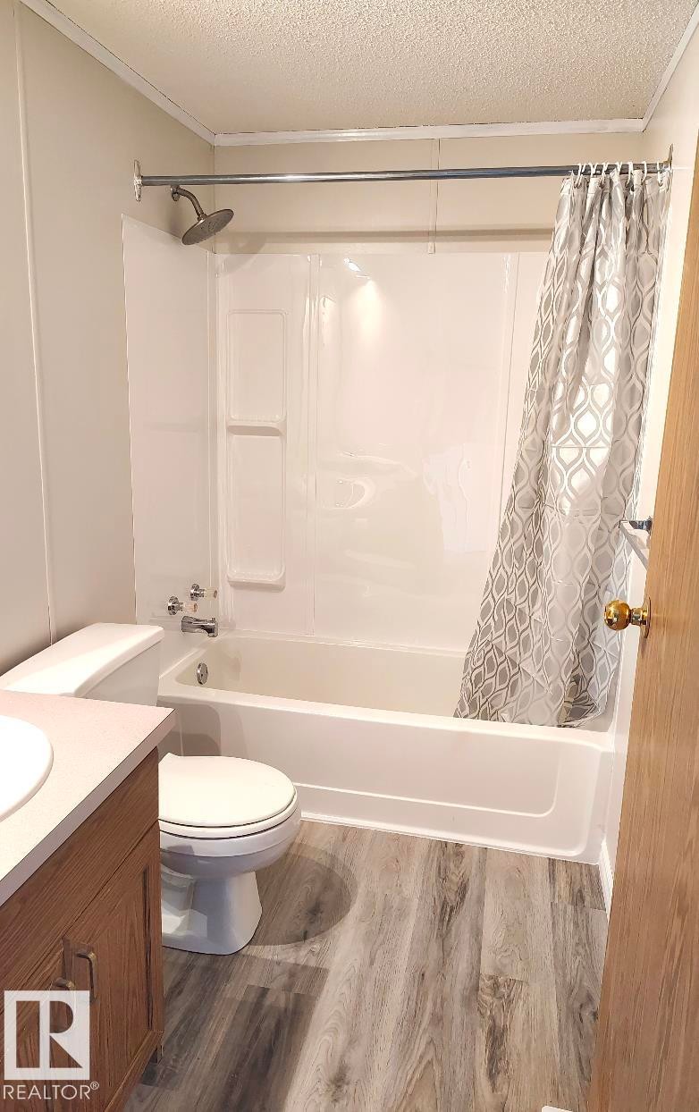 Bathroom with wood-finish flooring, white tub and shower surround, and a wood-finish vanity with a light-toned countertop - 4819 51 Avenue, Millet, AB - Indoor Photo Showing Bathroom