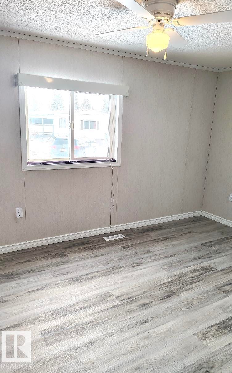 Room with wood-finish flooring, a window with a valance, and a ceiling fan with integrated lighting - 4819 51 Avenue, Millet, AB - Indoor Photo Showing Other Room
