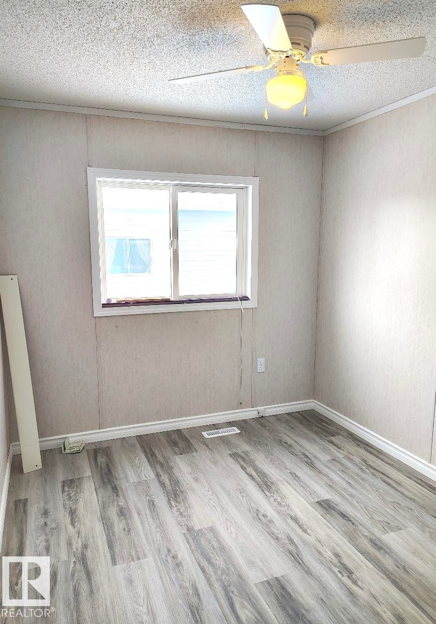 Interior space featuring wood-finish flooring, a white trim window, a ceiling fan with integrated lighting, and baseboard trim - 4819 51 Avenue, Millet, AB - Indoor Photo Showing Other Room