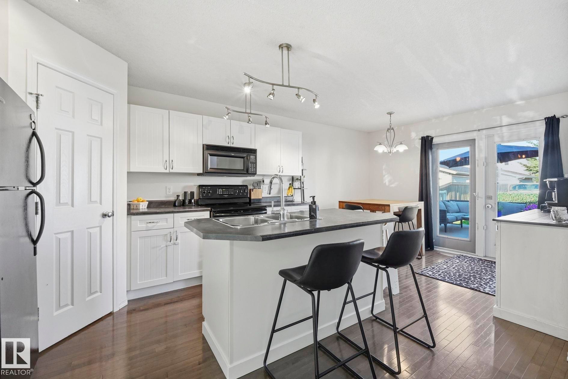 Kitchen featuring white cabinetry, dark countertops, built-in microwave, stainless steel sink, and wood-finish flooring - 215 85 Street Sw, Edmonton, AB - Indoor Photo Showing Kitchen With Upgraded Kitchen
