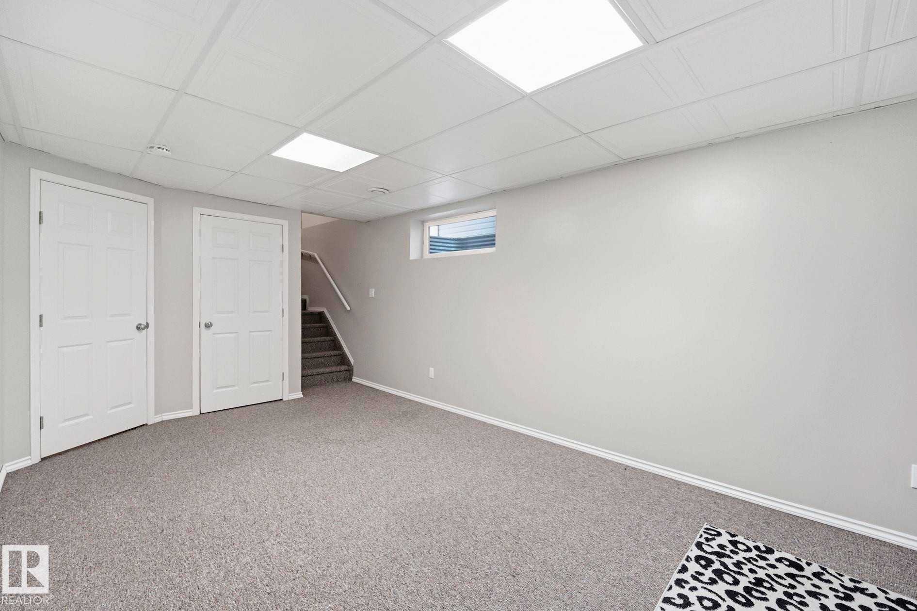 Spacious room featuring light gray walls, plush gray carpeting, and a white drop ceiling with recessed lighting - 215 85 Street Sw, Edmonton, AB - Indoor Photo Showing Basement