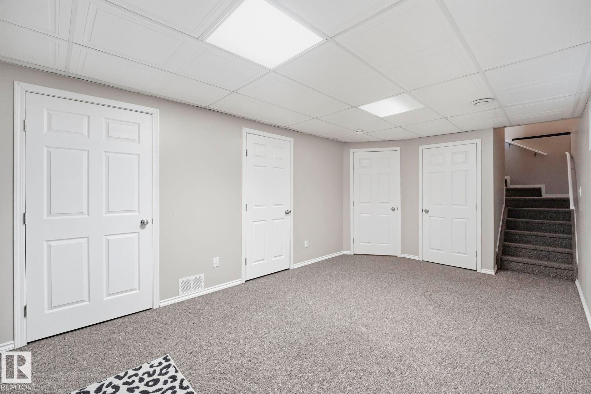 Spacious room featuring light gray walls, gray carpeting, and multiple white six-panel doors - 215 85 Street Sw, Edmonton, AB - Indoor Photo Showing Other Room