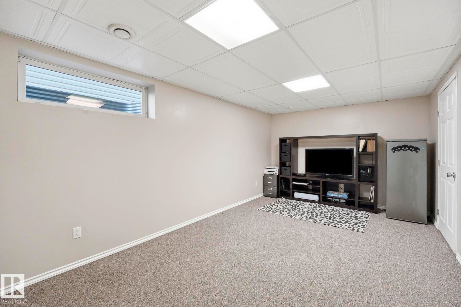 Carpeted recreation room featuring an egress window, drop ceiling with recessed lighting, and painted walls - 215 85 Street Sw, Edmonton, AB - Indoor Photo Showing Basement