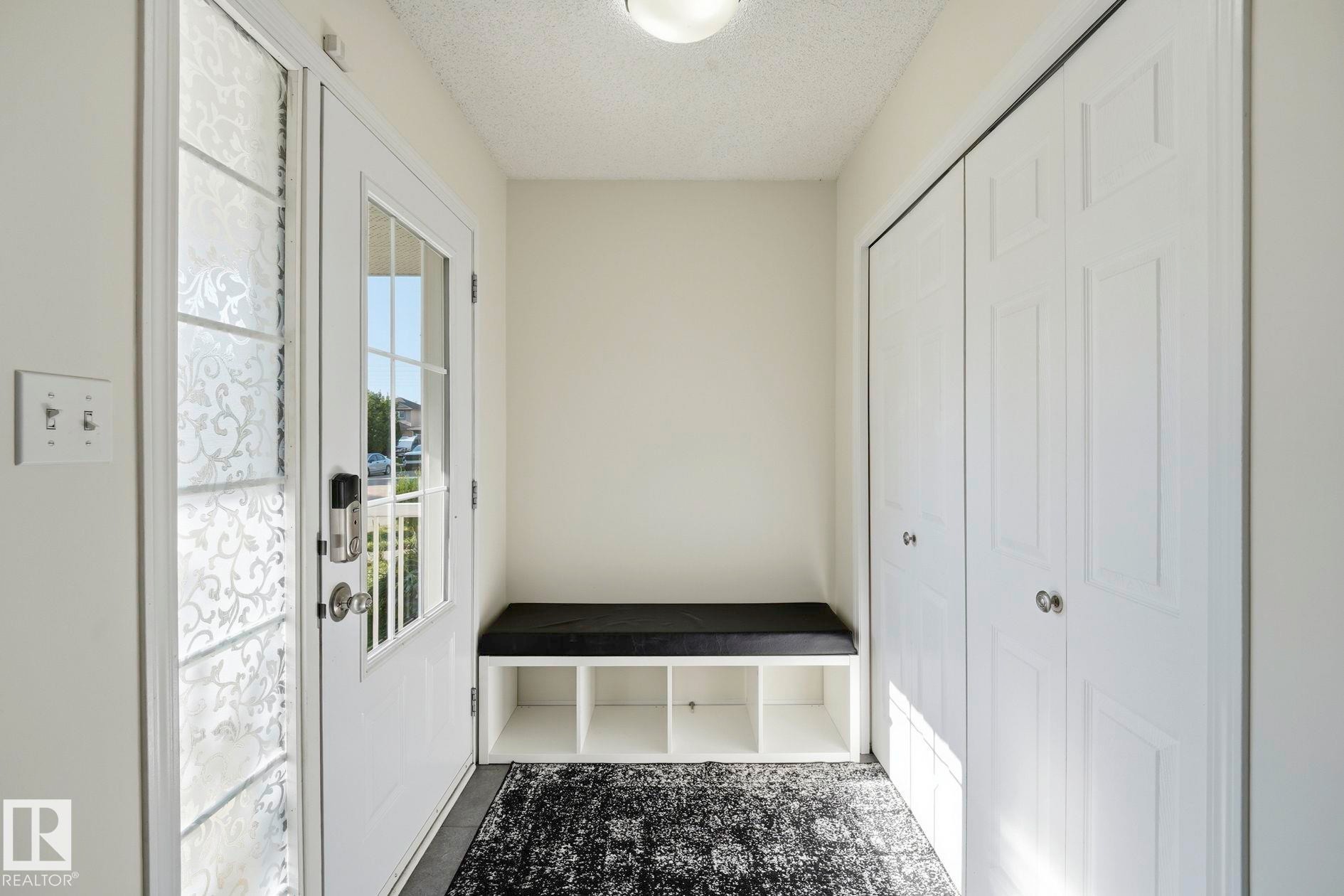 Entryway featuring a white paneled door with glass inserts, a built-in storage bench, and bi-fold closet doors - 215 85 Street Sw, Edmonton, AB - Indoor Photo Showing Other Room